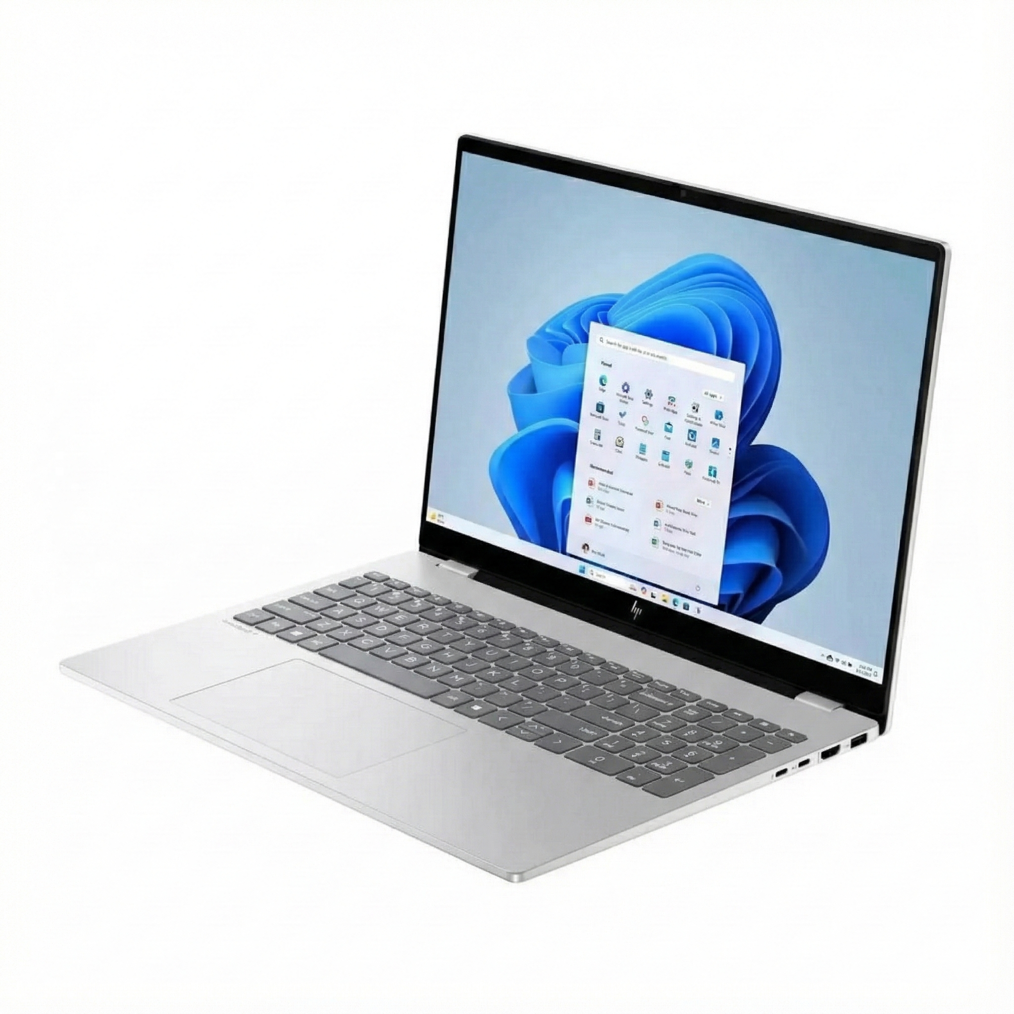 Windows 11 arayüzüne sahip gümüş dizüstü bilgisayar. Ekran mavi soyut şekiller ve uygulama simgeleri gösteriyor. Klavye görünür.