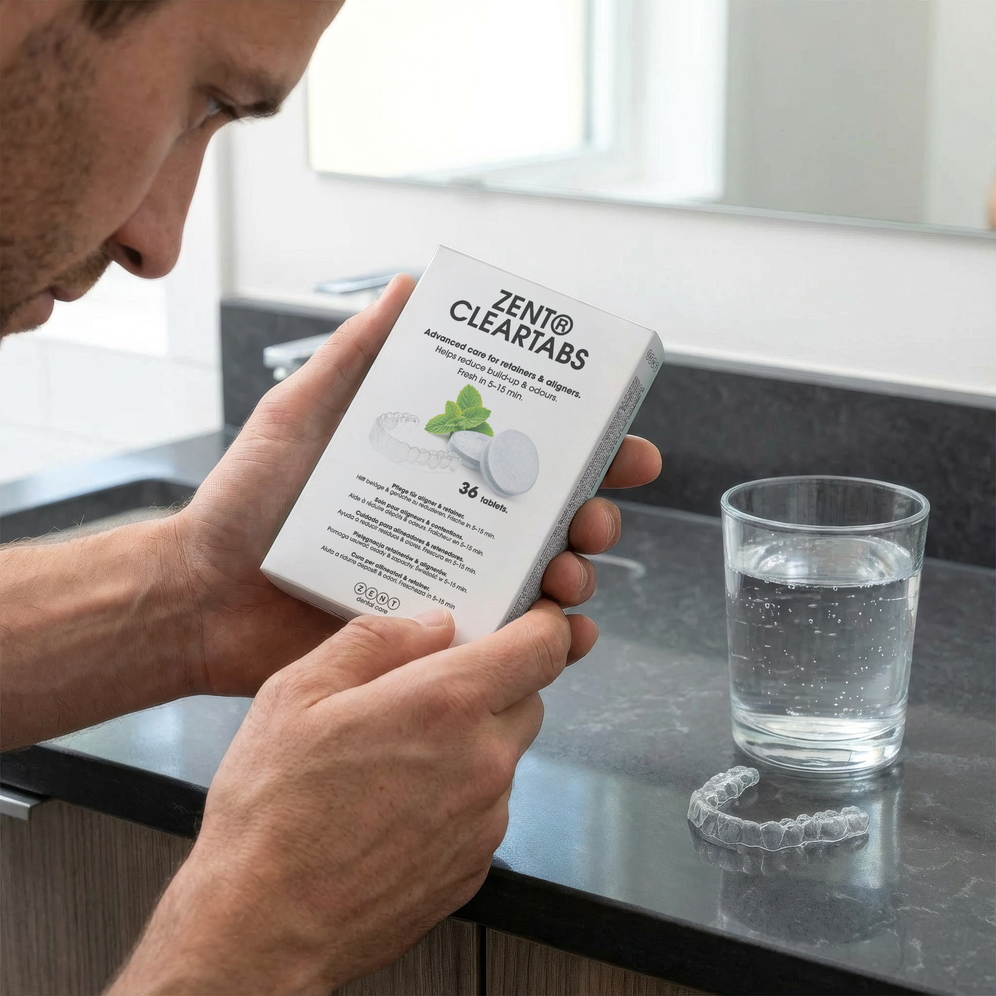 Mężczyzna trzyma pudełko ClearTabs, szklankę wody i aligner na blacie w łazience.