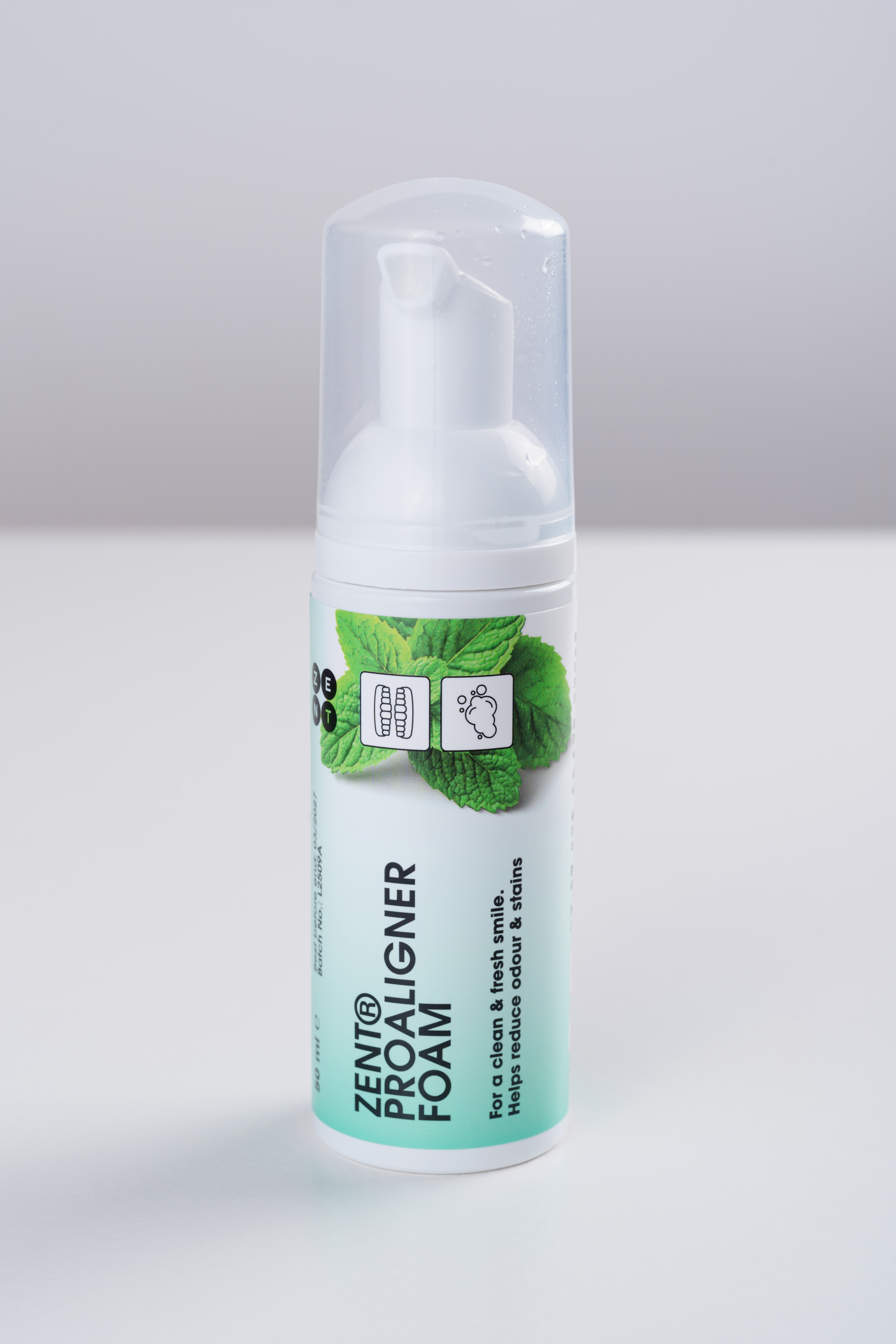 Biała butelka pianki ZENT Proaligner. Ma wzór liścia mięty i tekst: 'Dla czystego i świeżego uśmiechu'.