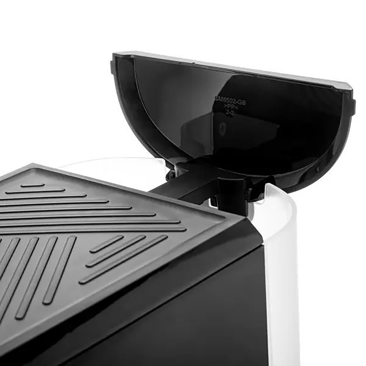 Un primo piano di una macchina da caffè in bianco e nero con coperchio nero aperto. La parte superiore ha una superficie strutturata. Lo sfondo è bianco.