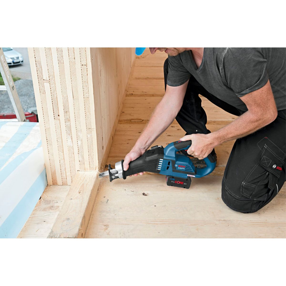 Ein Mann benutzt eine blau-schwarze Säbelsäge, um Holz zu schneiden. Er kniet in einer Holzkonstruktion.