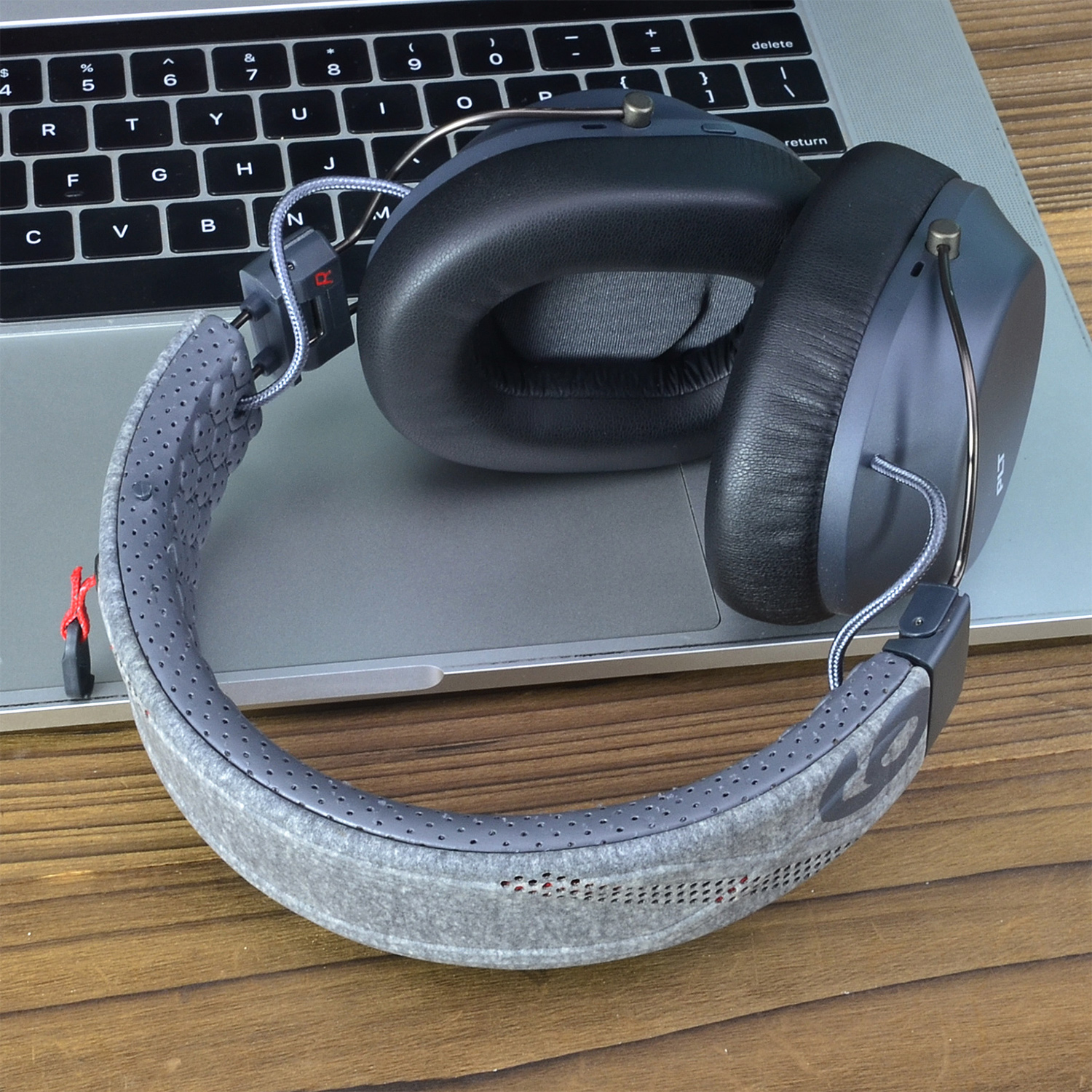 Słuchawki leżą na klawiaturze laptopa na drewnianej powierzchni. Słuchawki są szare i czarne.