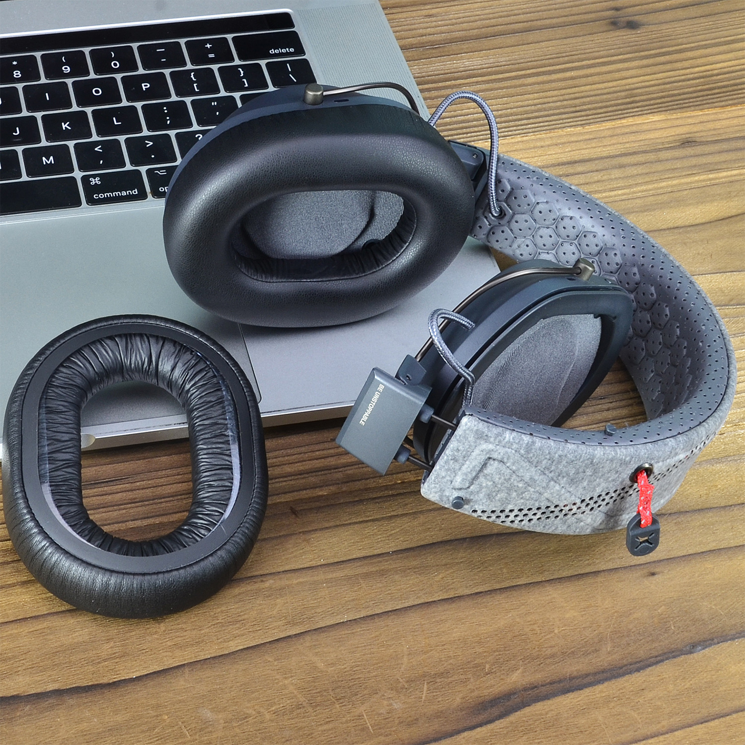 Słuchawki z zapasową wkładką douszną leżą na klawiaturze laptopa. Słuchawki są czarne i szare, z czerwoną zawieszką.