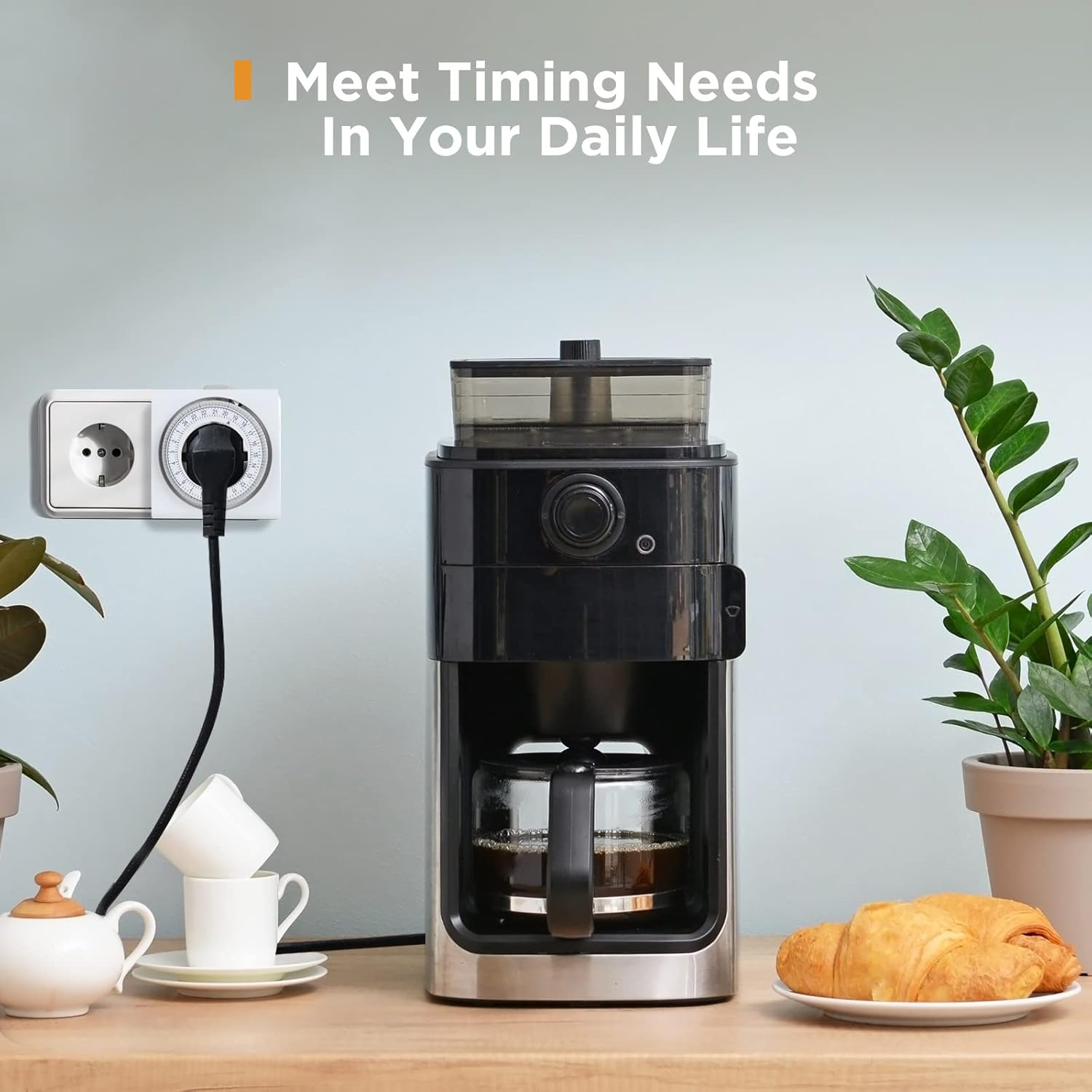 Kaffeemaschine, Timer, Tassen, Croissant und Pflanzen stehen auf einem Tisch. Die Kaffeemaschine ist schwarz und silber.