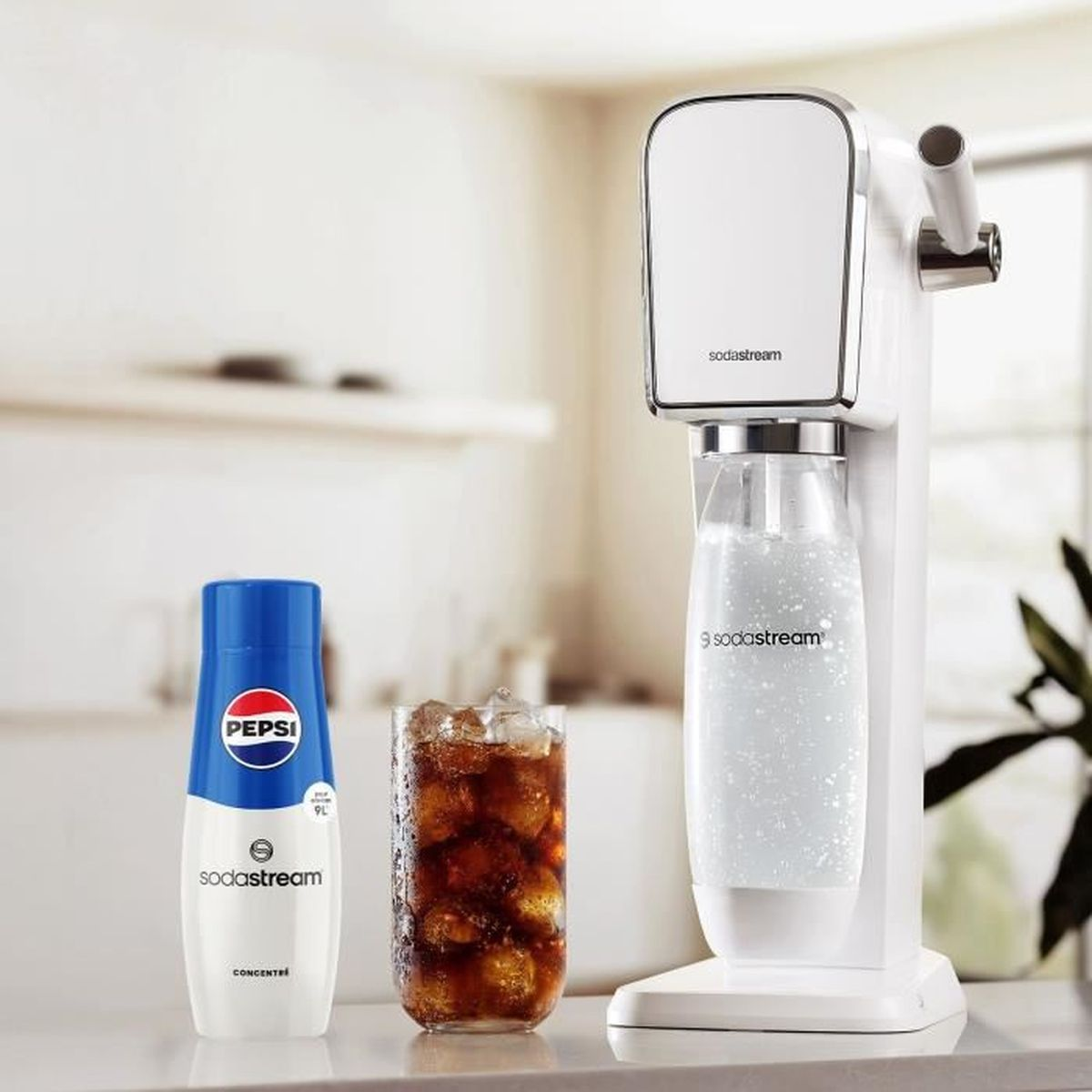 Una macchina Sodastream, una bottiglia di concentrato Pepsi e un bicchiere di cola con cubetti di ghiaccio su un tavolo.
