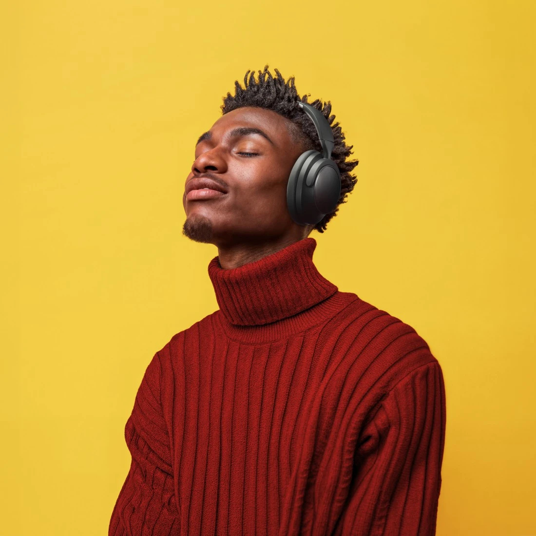 Czarny mężczyzna w słuchawkach i czerwonym golfie z zamkniętymi oczami na żółtym tle.