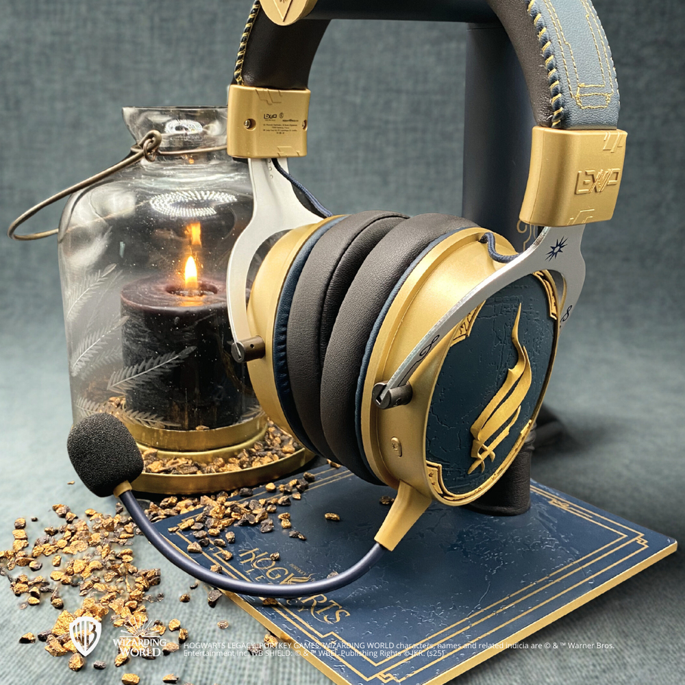 Goldenes und marineblaues Headset auf einem Ständer, mit einer brennenden Kerze in einem Glas. Steine und ein Buch mit dem Hogwarts-Logo im Vordergrund.