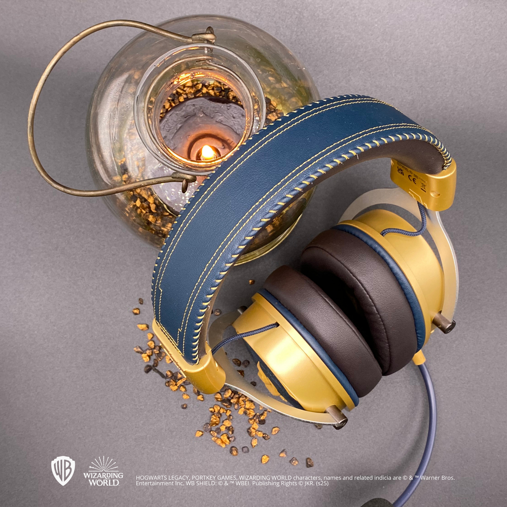 Goldene und blaue Kopfhörer mit einem Glasbehälter und einer brennenden Kerze auf grauem Untergrund.