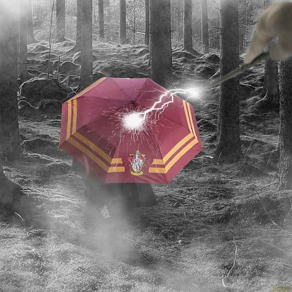 Un paraguas rojo con rayas doradas es alcanzado por un rayo en un bosque. Una varita lanza el hechizo. El paraguas tiene un escudo.