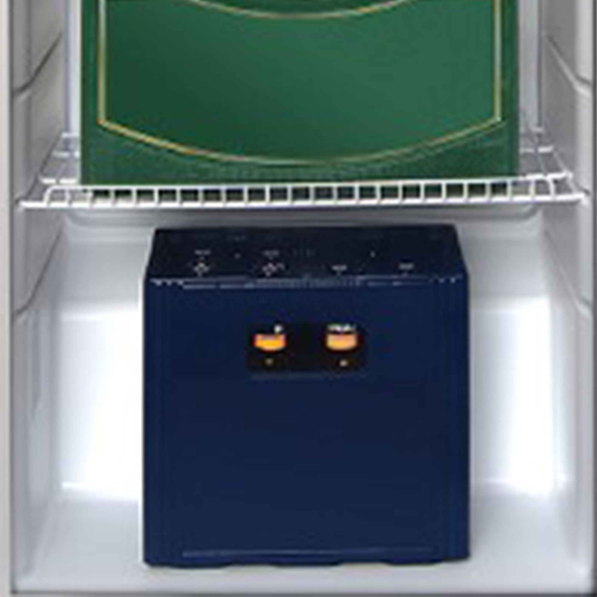 Ein Kühlschrank mit einer grünen Kiste auf dem oberen Regal und einem blauen Gerät mit Lichtern auf dem unteren Regal.