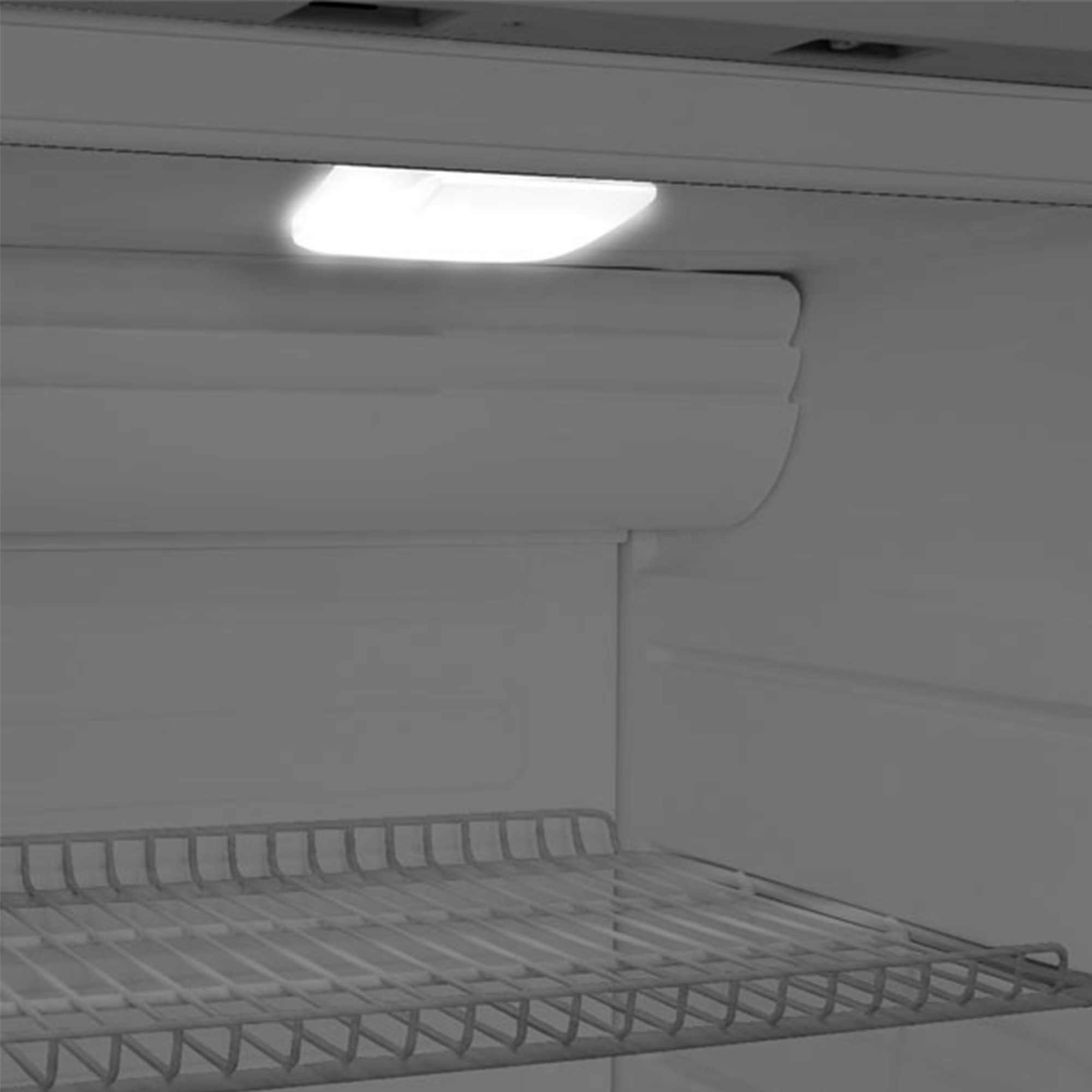 Im Inneren eines Kühlschranks. Ein helles Licht leuchtet die Oberseite aus. Metallrost am Boden. Graue Innenausstattung.