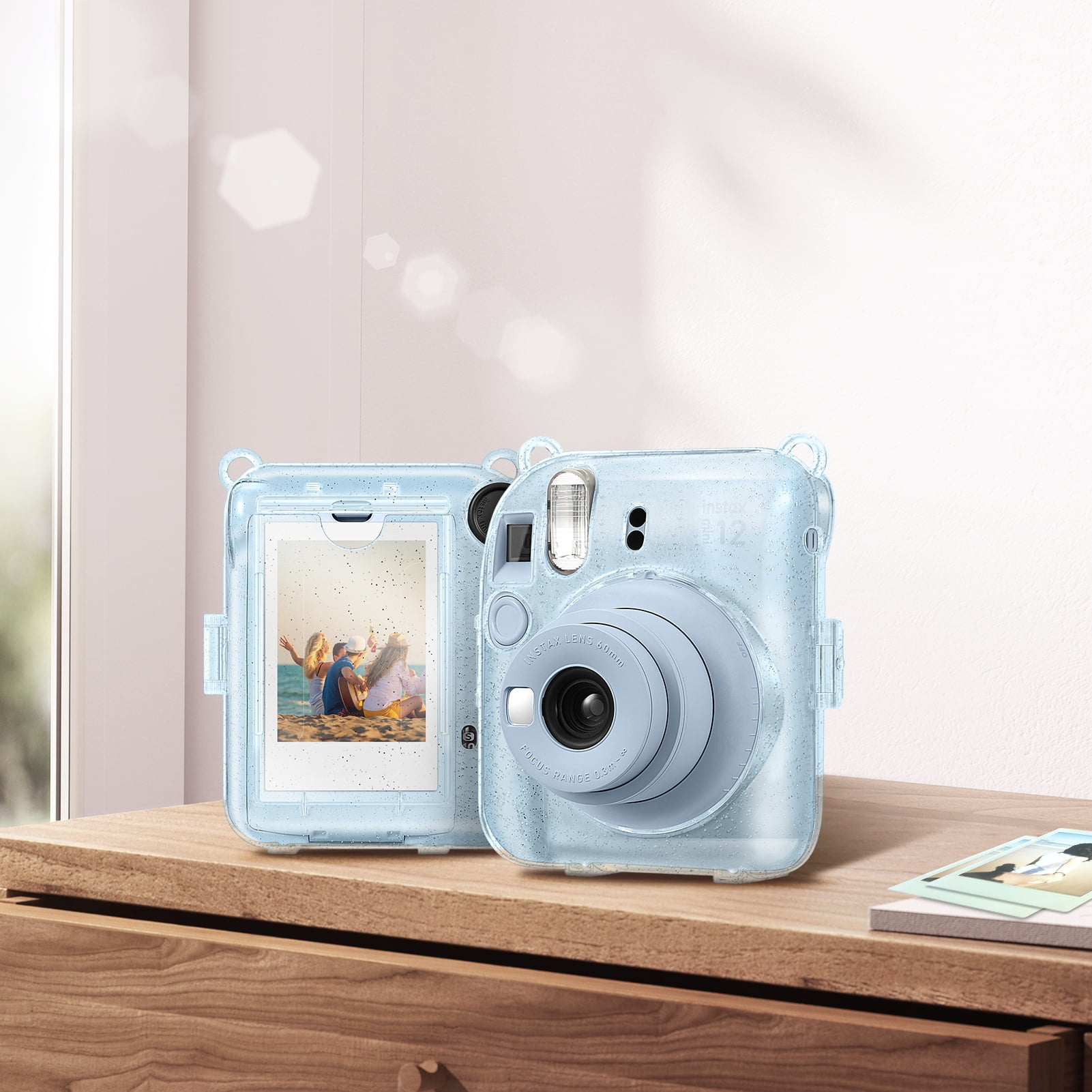 Eine hellblaue Instax-Kamera mit Hülle. Die Hülle zeigt ein Foto von Menschen am Strand. Sie steht auf einer Holzoberfläche.