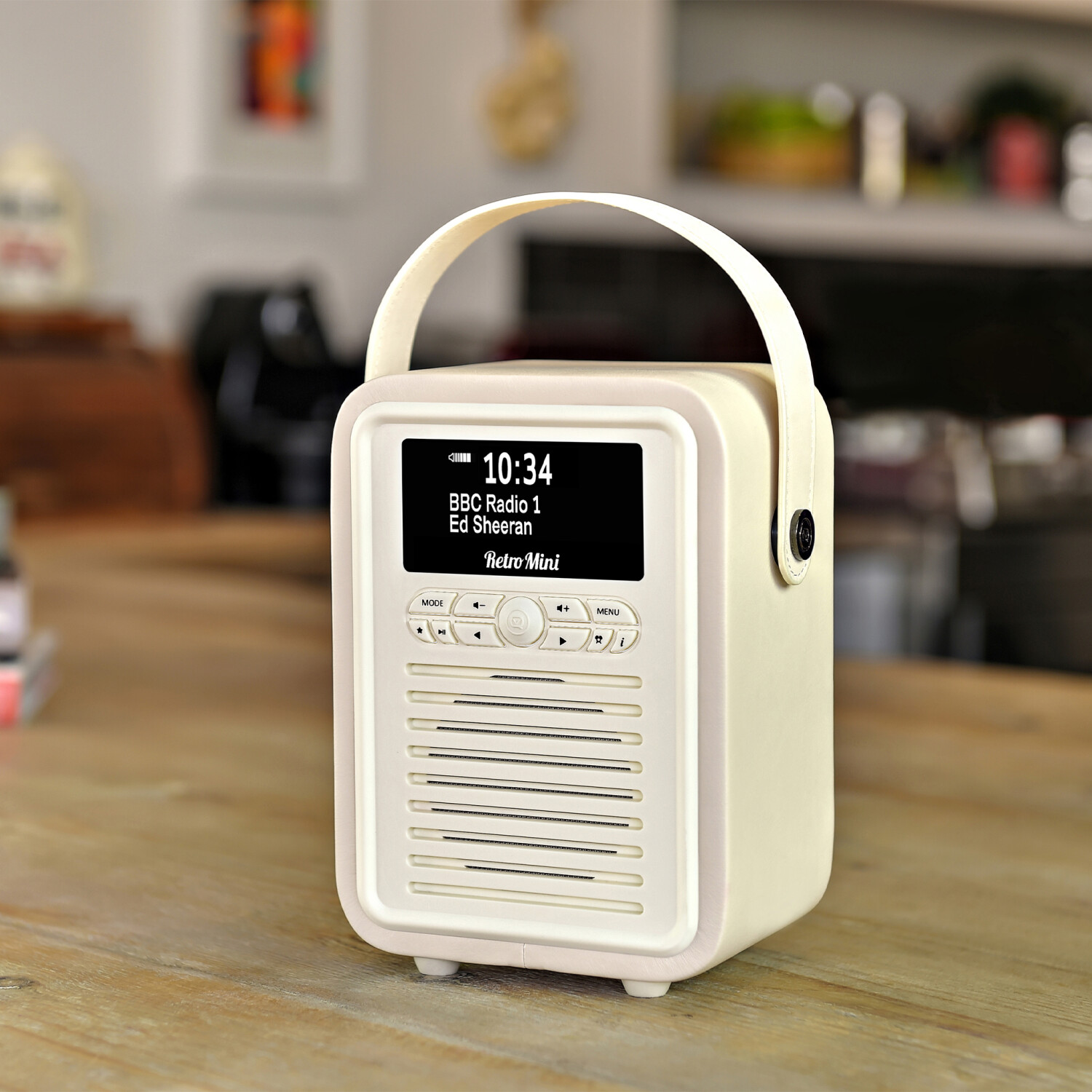 Cremefarbenes Retro-Radio auf einem Holztisch. Der Bildschirm zeigt Uhrzeit und Radiosender an. Griff ist hochgeklappt. Verschwommener Hintergrund einer Küche.
