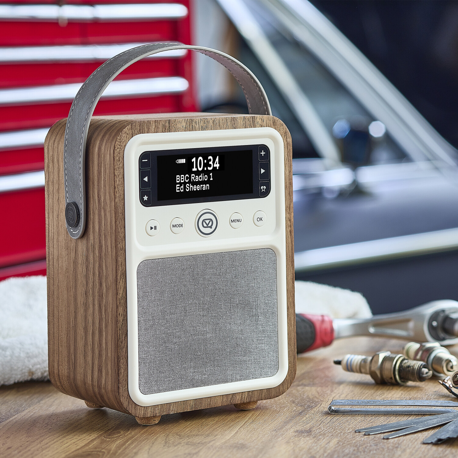 Holzradio mit Griff. Der Bildschirm zeigt die Uhrzeit und den Radiosender. Verschiedene Werkzeuge befinden sich im Vordergrund.