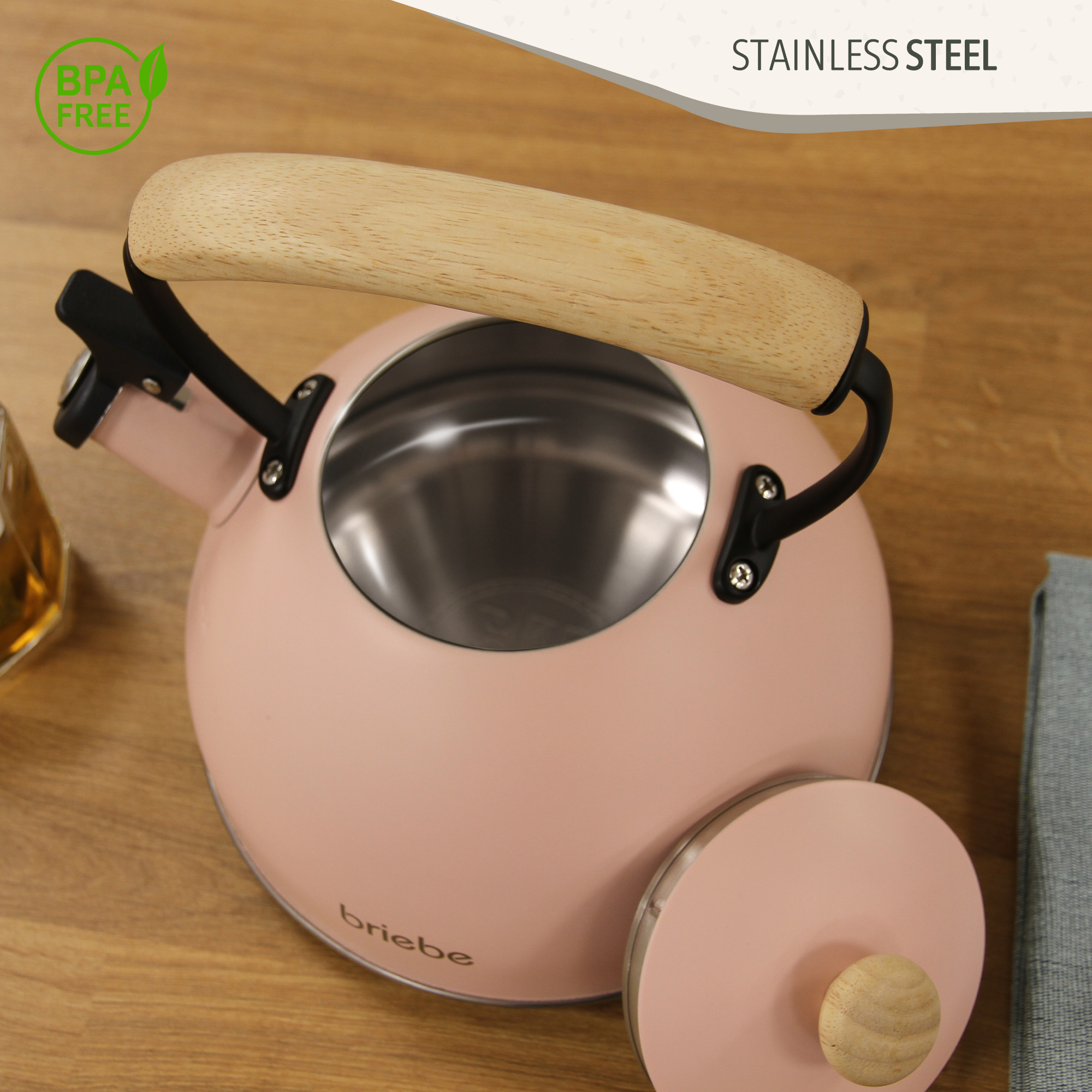 Hervidor rosa con mango y tapa de madera. Acero inoxidable. Etiqueta libre de BPA. Sobre superficie de madera con tela.