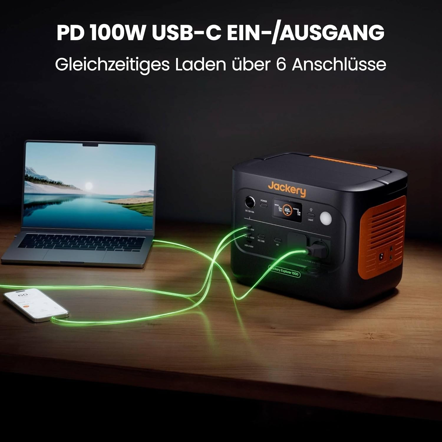 Ein Laptop, ein Telefon und eine Powerstation sind durch leuchtend grüne Kabel verbunden. Die Powerstation ist schwarz und orange, mit der Marke Jackery.