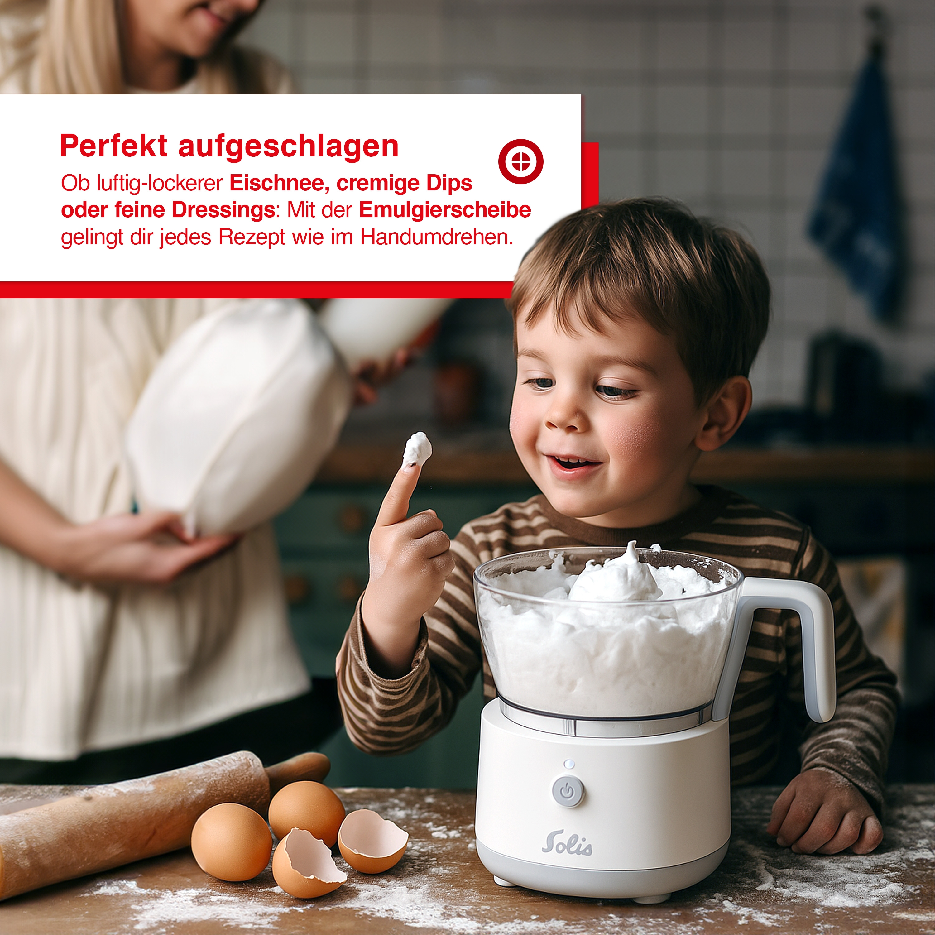 Un bambino sorride, indicando la panna montata da un robot da cucina. Uova, farina e un mattarello sul tavolo.