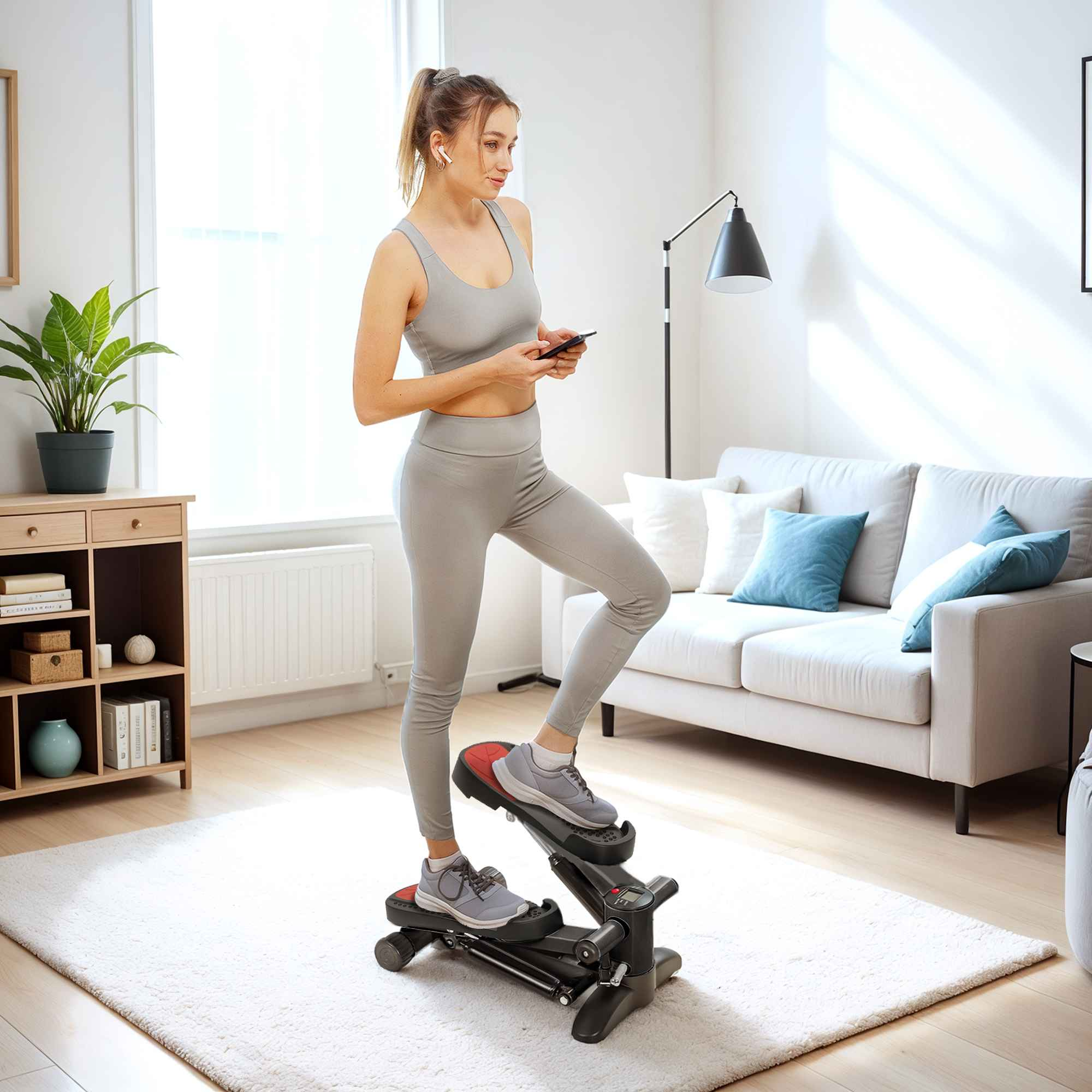 Frau in grauer Sportkleidung benutzt ein Stepper-Gerät. Sie hält ein Telefon, Ohrhörer im Wohnzimmer.