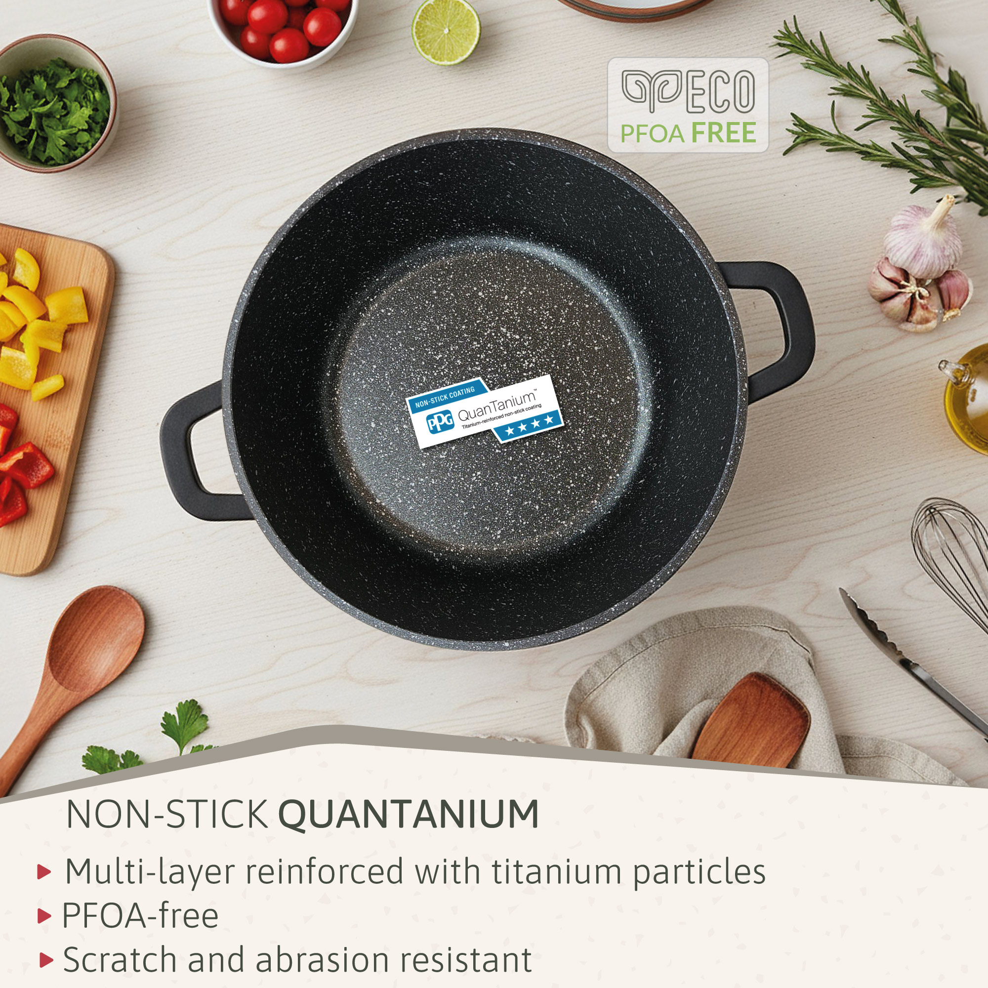Una sartén Quantanium antiadherente está rodeada de ingredientes como tomates, hierbas, ajo y una cuchara de madera, sobre una superficie de madera.