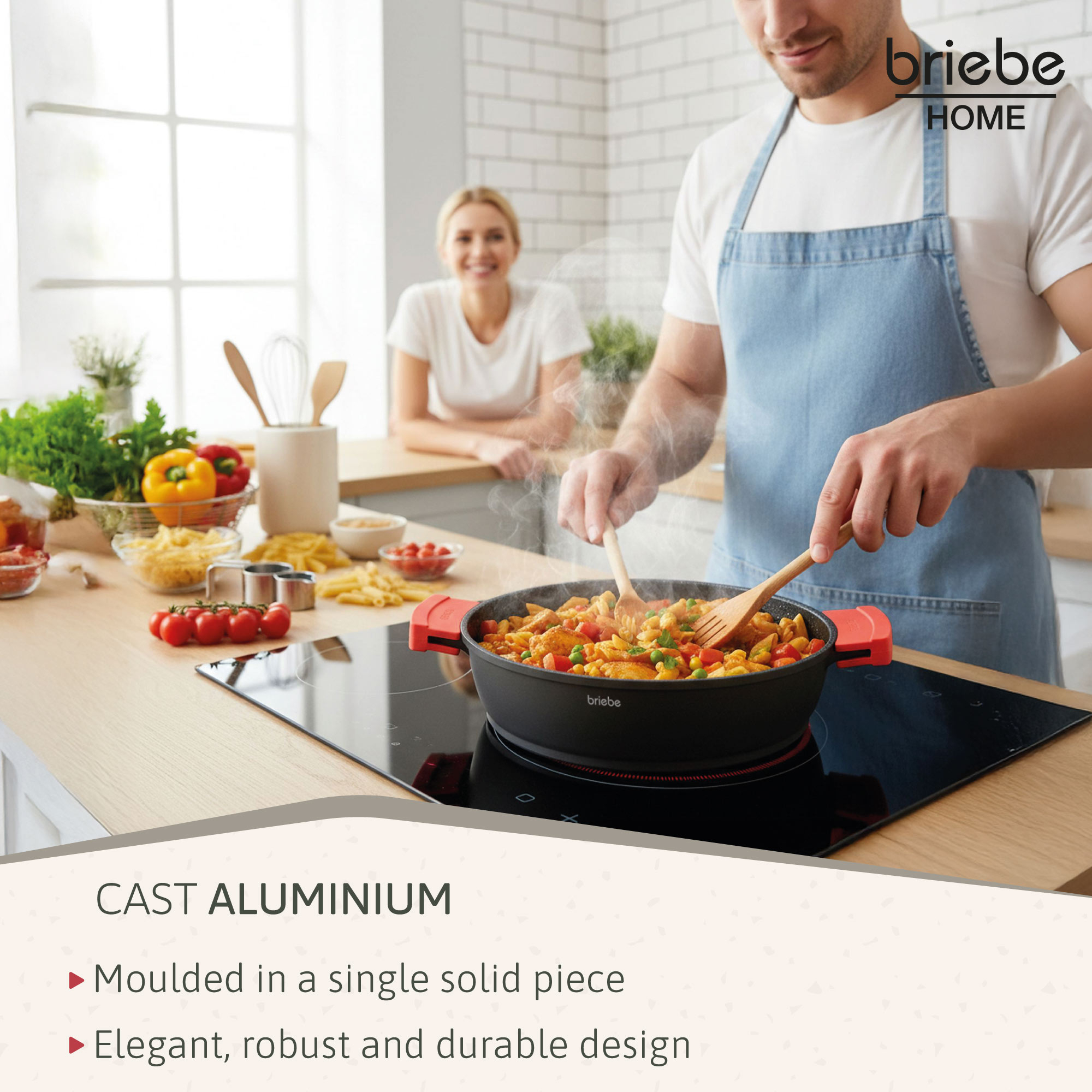 Un hombre cocina en una sartén negra, una mujer observa. Verduras y pasta en la mesa. La sartén es de briebe HOME.