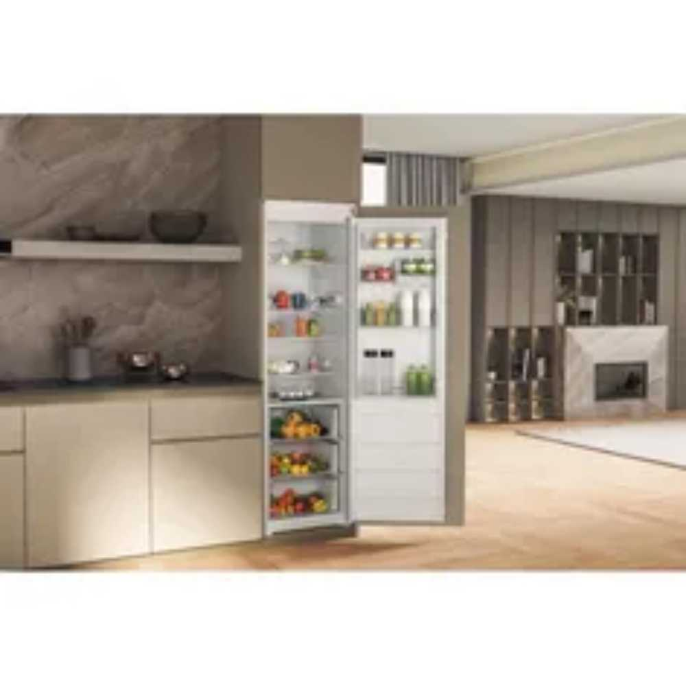 Een keuken met een open koelkast vol eten. Kasten en aanrecht zijn zichtbaar. De achtergrond toont een woonkamer.