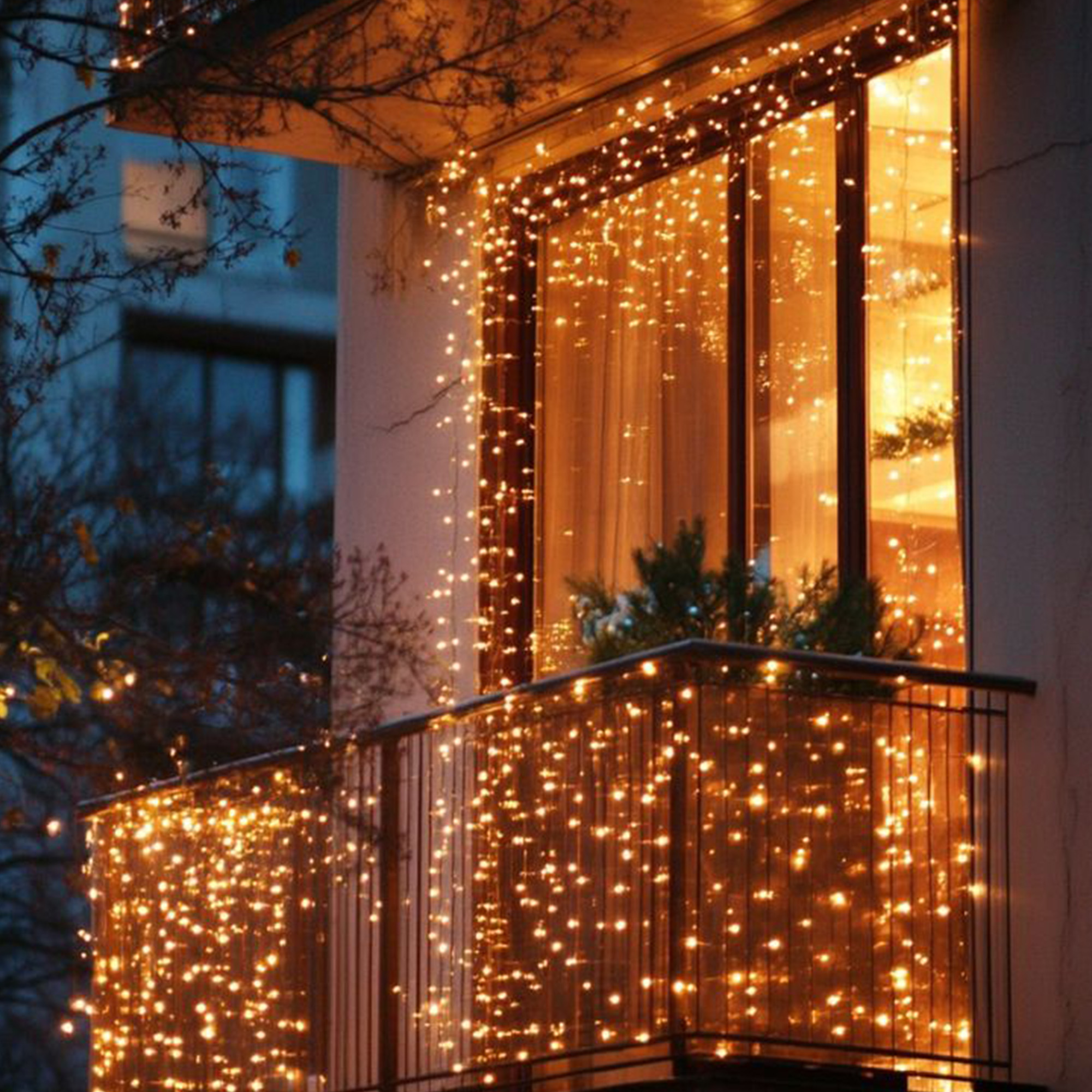 Balcón decorado con luces cálidas. Ventana detrás. Las luces cuelgan del techo y la barandilla.