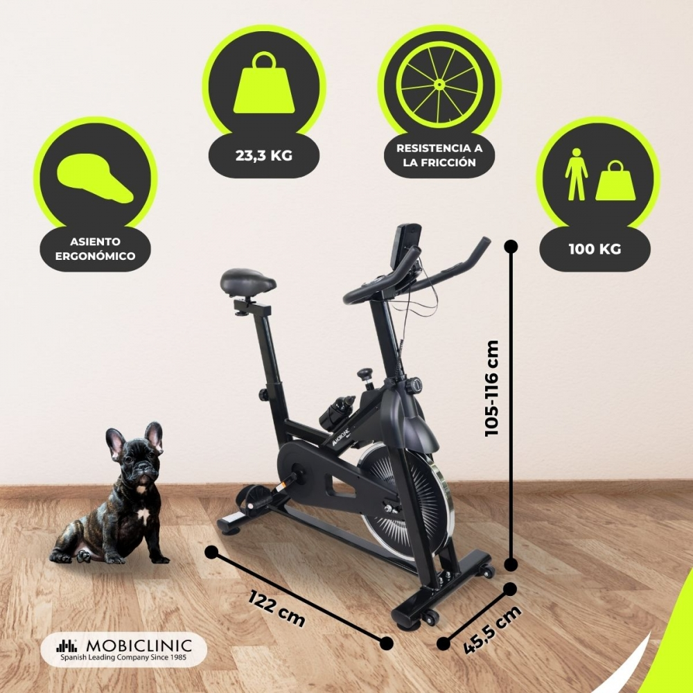 Una bicicleta de ejercicios negra con detalles de dimensiones y peso, un perro pequeño sentado a la izquierda. Información en español.