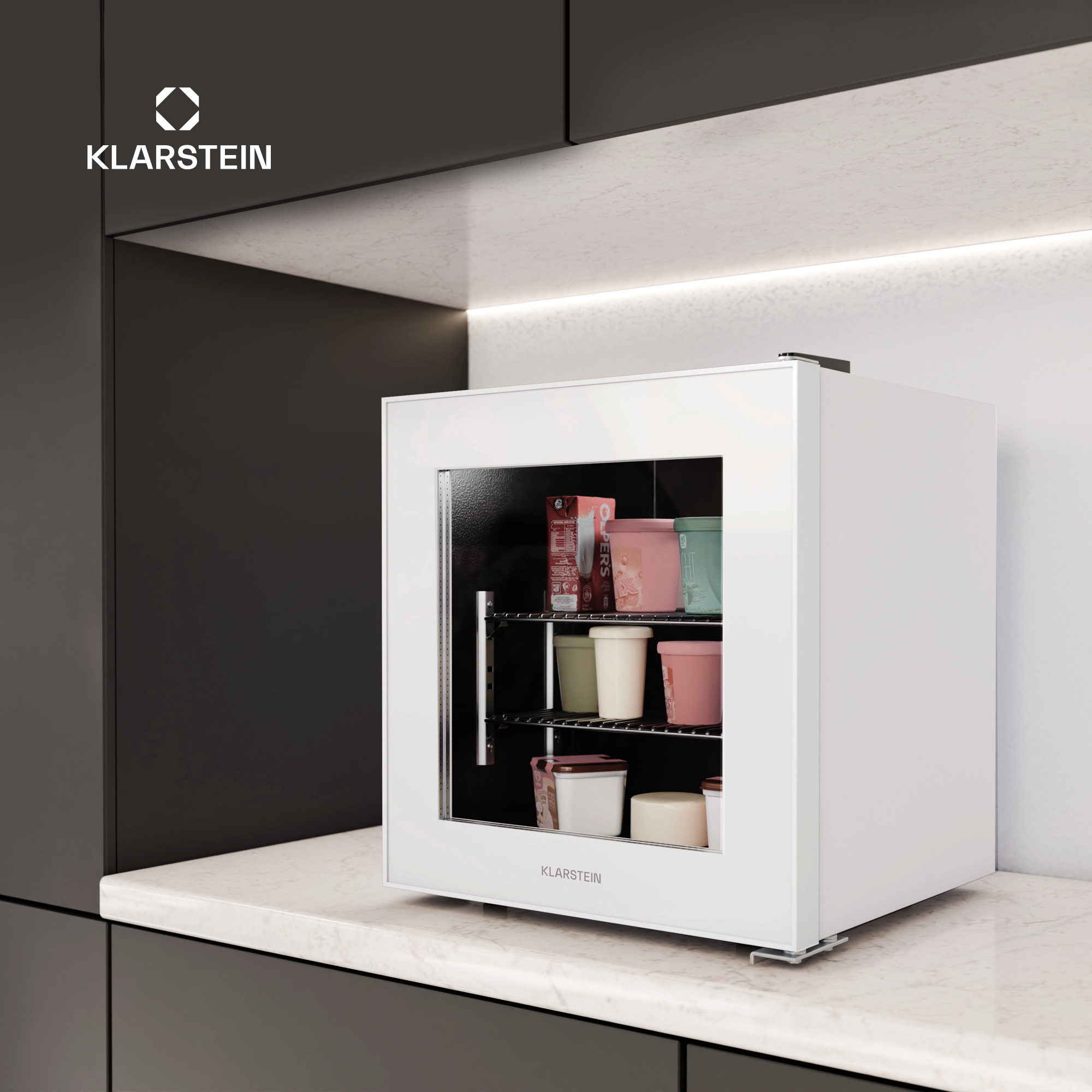 Un mini-frigorifero Klarstein bianco su un piano di lavoro, pieno di contenitori. Lo sfondo è armadi scuri e parete bianca.