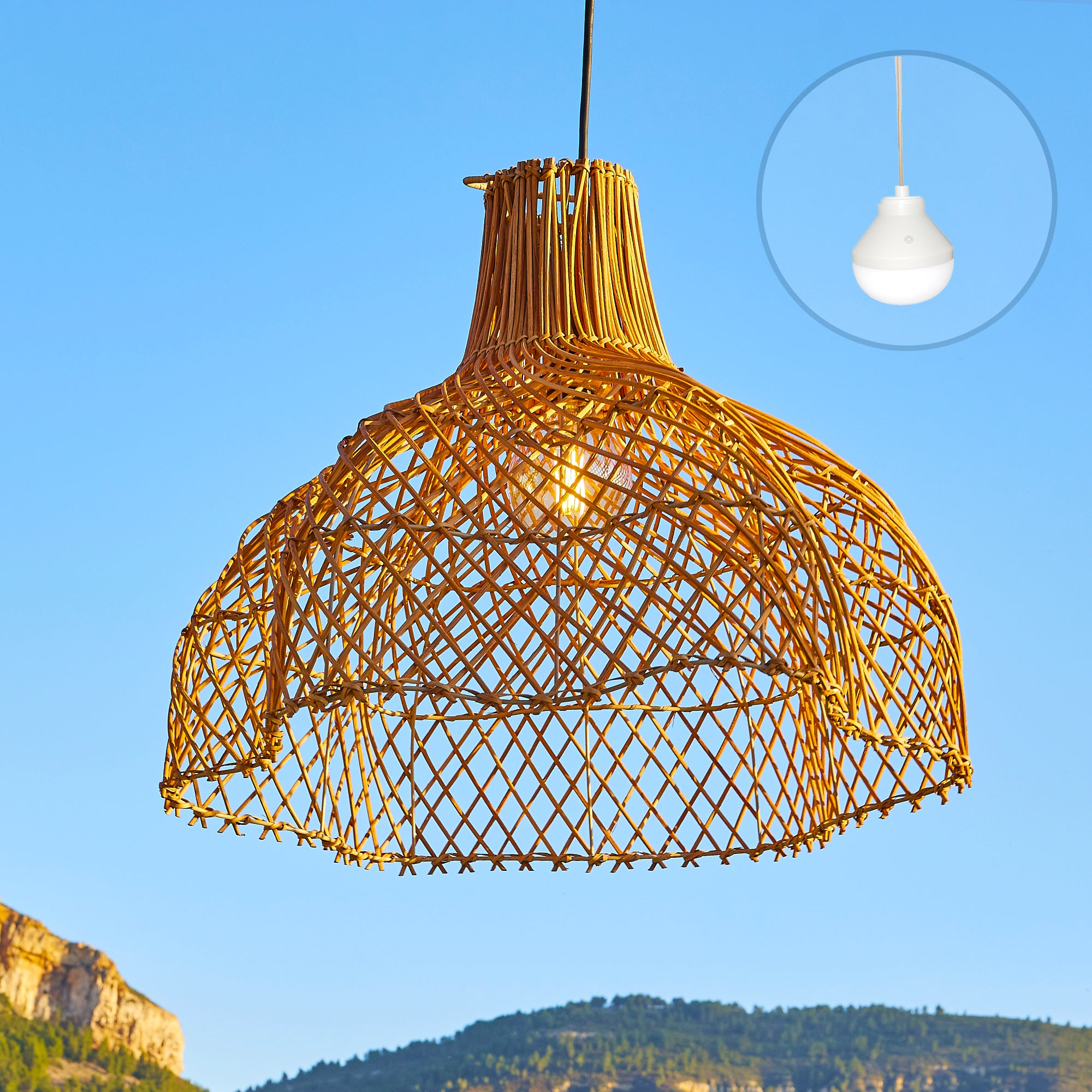 Wicker-Lampenschirm, der vor blauem Himmel hängt. Im Hintergrund befindet sich eine Glühbirne. Berge in der Ferne.