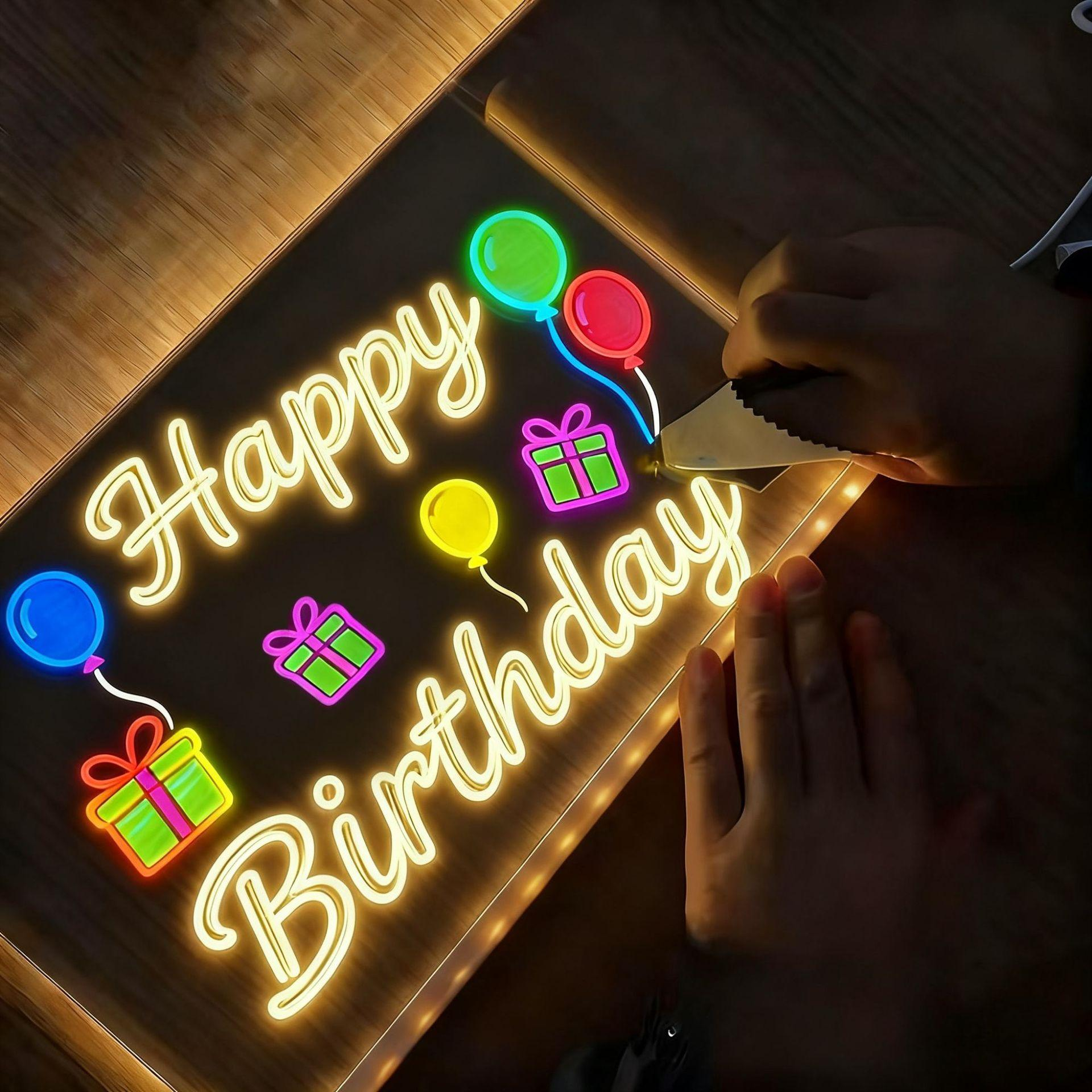 Ein Neon-Schild sagt Happy Birthday mit Ballons und Geschenken. Hände halten ein Werkzeug in der Nähe des Schildes auf einer Holzoberfläche.