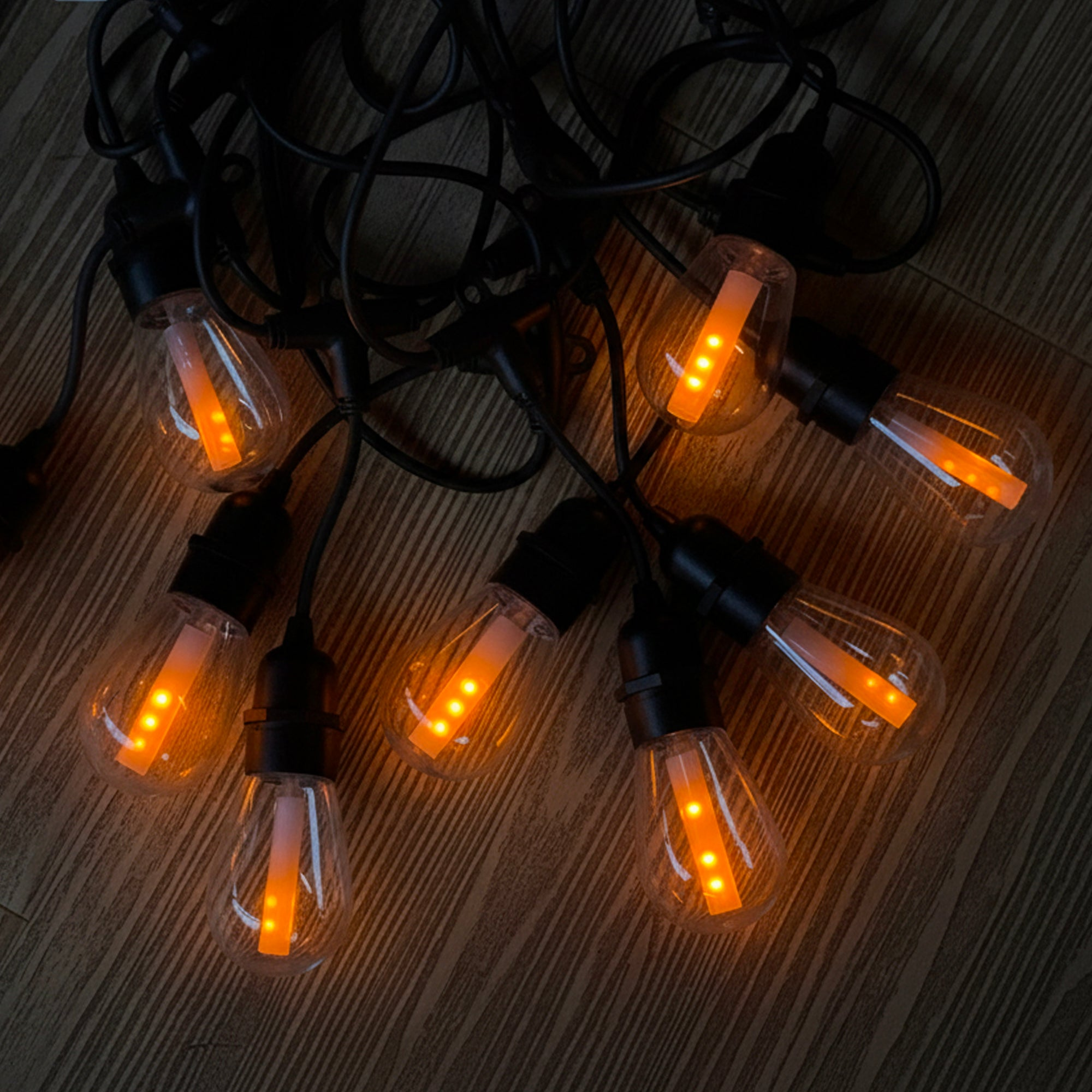 Eine Lichterkette mit leuchtenden, durchsichtigen Glühbirnen mit schwarzen Drähten auf Holz. Birnen haben orangefarbene LEDs.