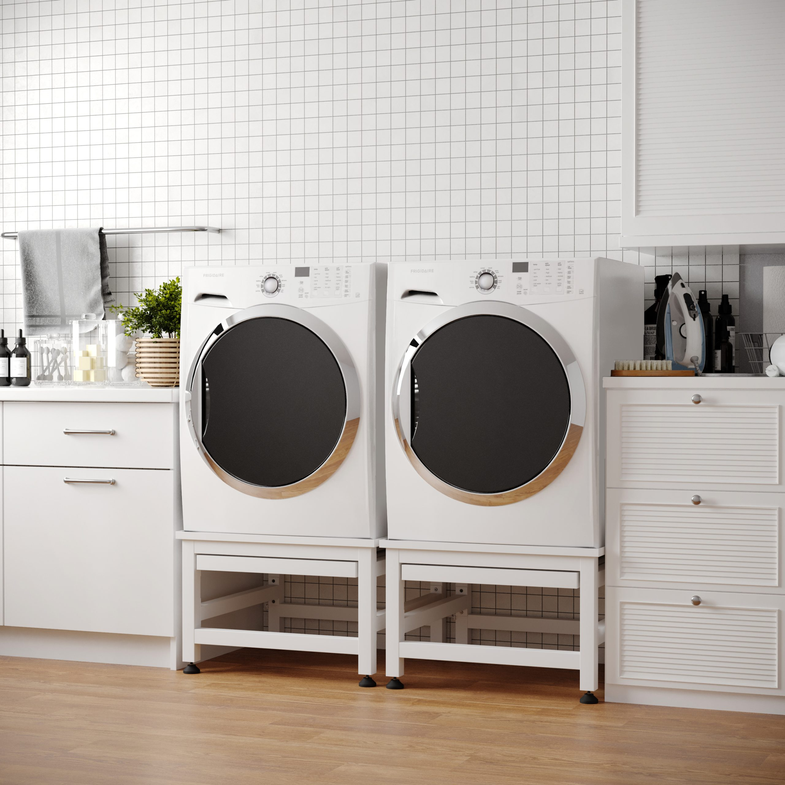 Waskamer met twee witte drogers, kasten en een betegelde muur. Inclusief een strijkijzer en schoonmaakartikelen.