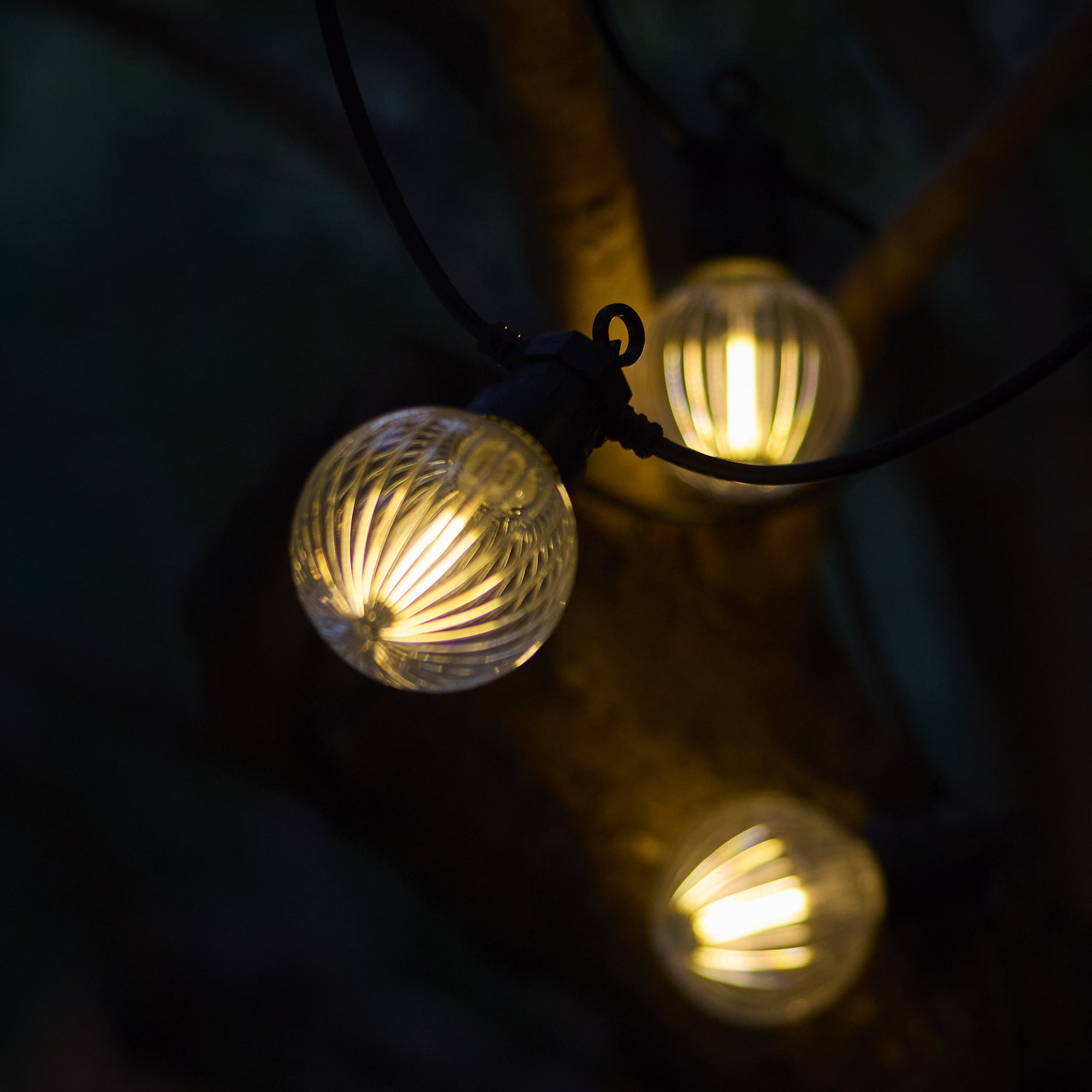 Nahaufnahme von drei leuchtenden Lichterketten mit dunklem Hintergrund. Die Lichter sind rund und klar.