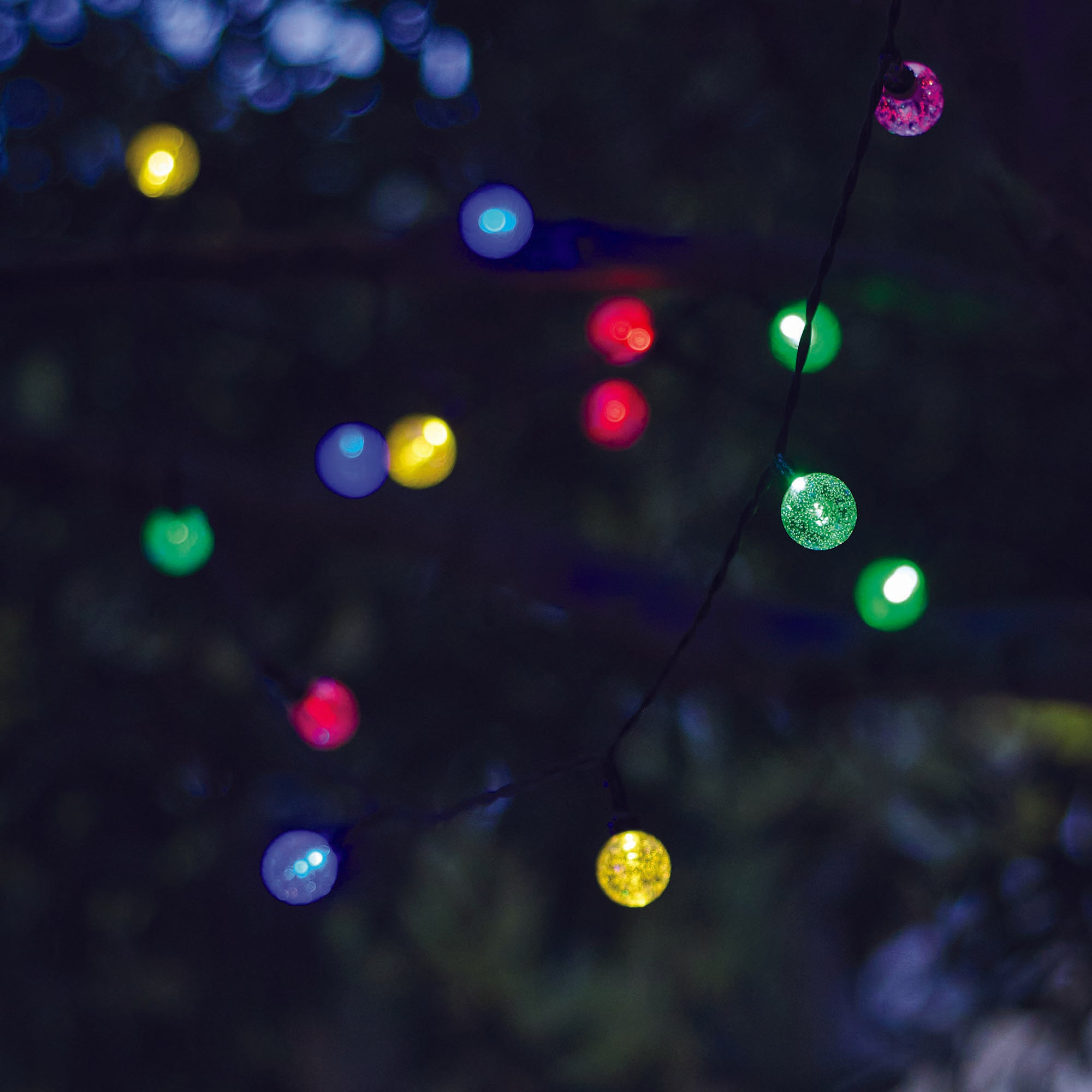 Eine Lichterkette mit bunten Lichtern vor dunklem Hintergrund. Rote, blaue, grüne und gelbe Lichter sind sichtbar.