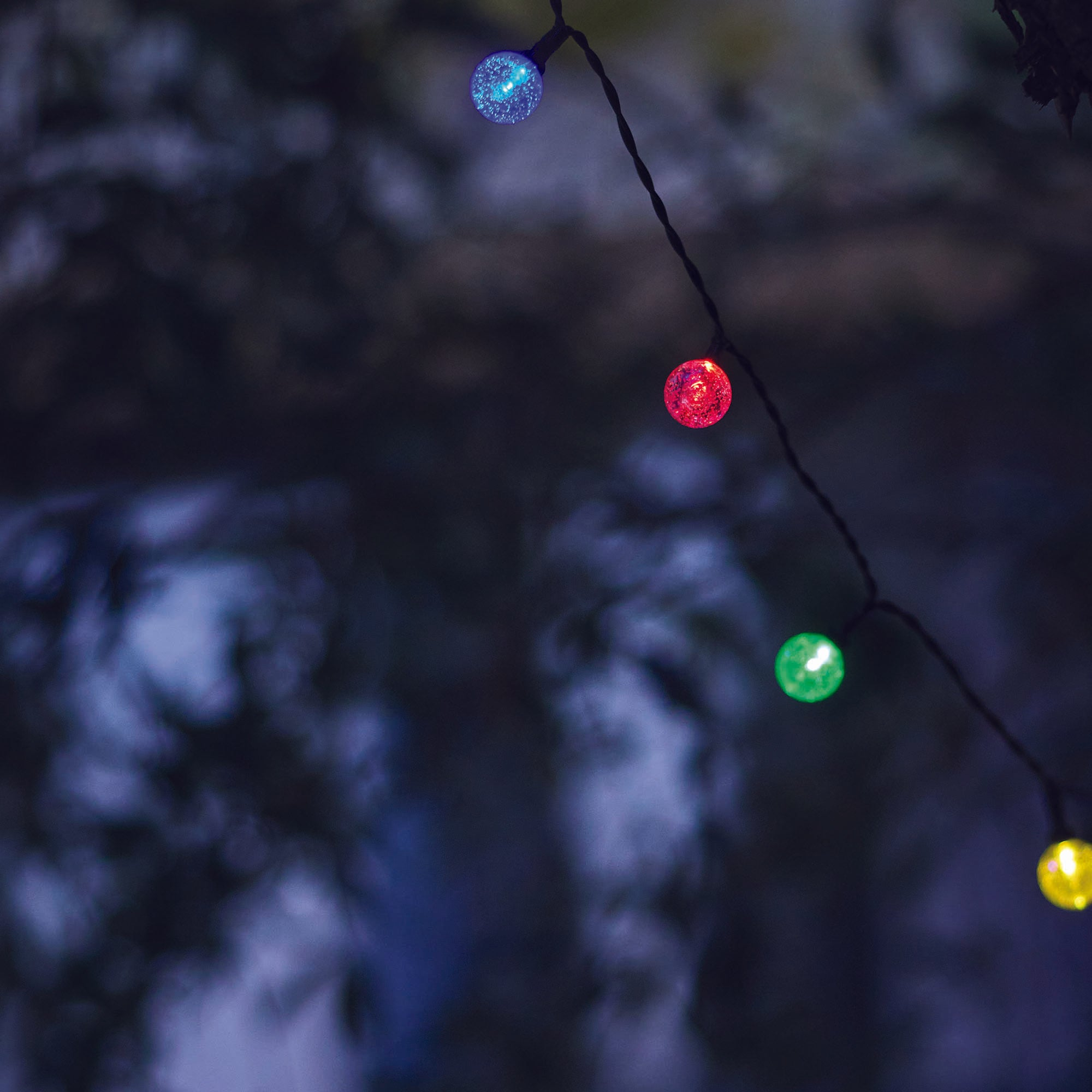 Eine Lichterkette mit bunten Lichtern auf dunklem Hintergrund. Blaue, rote, grüne und gelbe Lichter sind sichtbar.