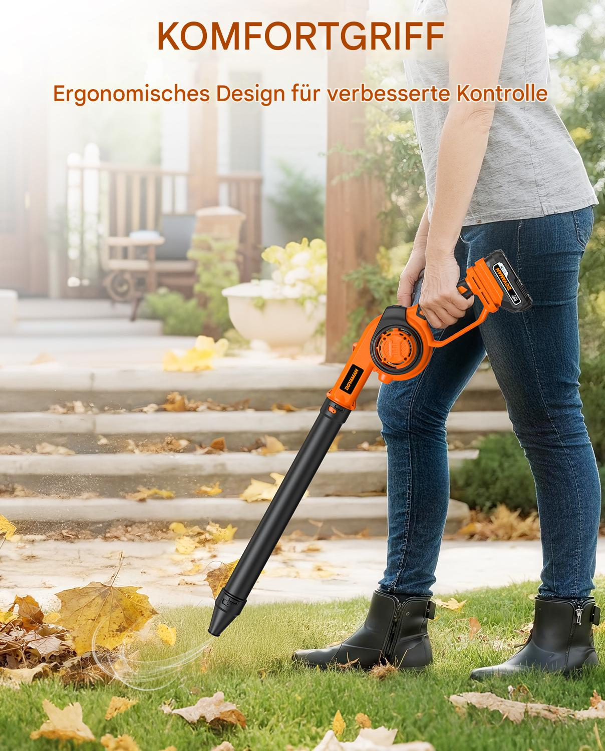 Eine Person benutzt ein orange-schwarzes Laubgebläse auf einem Rasen mit Herbstblättern. Im Hintergrund sind Haus und Treppe zu sehen.