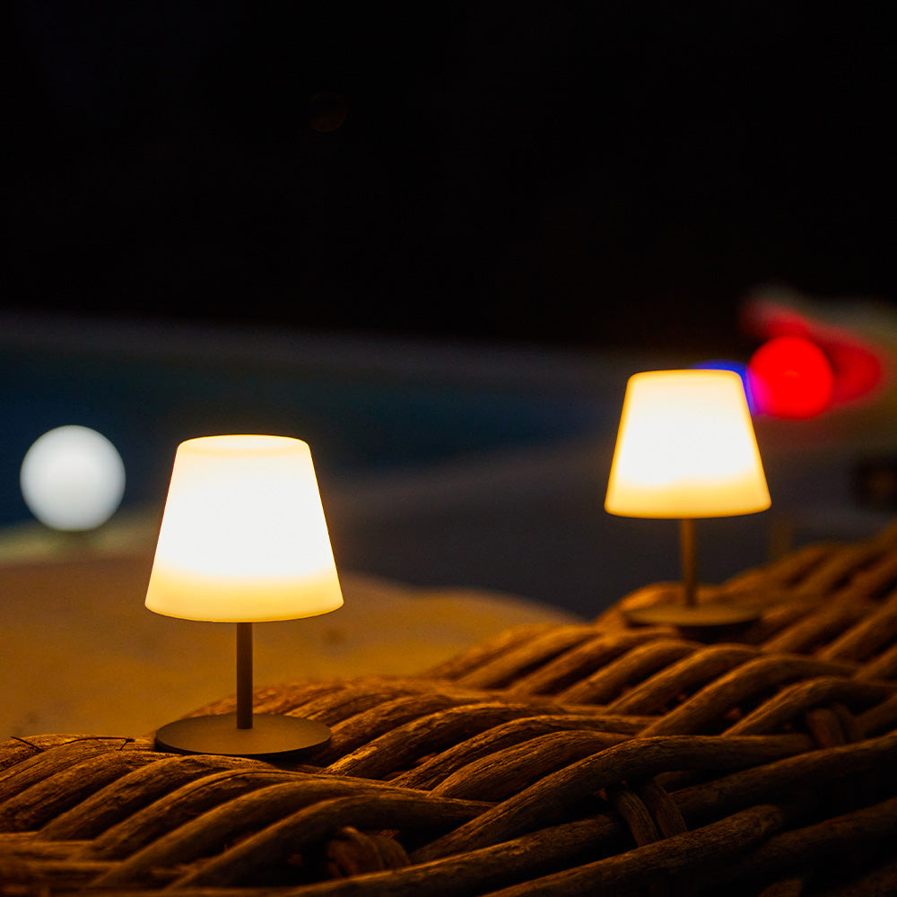 Zwei beleuchtete Lampen auf einer gewebten Oberfläche bei Nacht. Im Hintergrund sind eine weiße Kugel und verschwommene rote Lichter zu sehen.