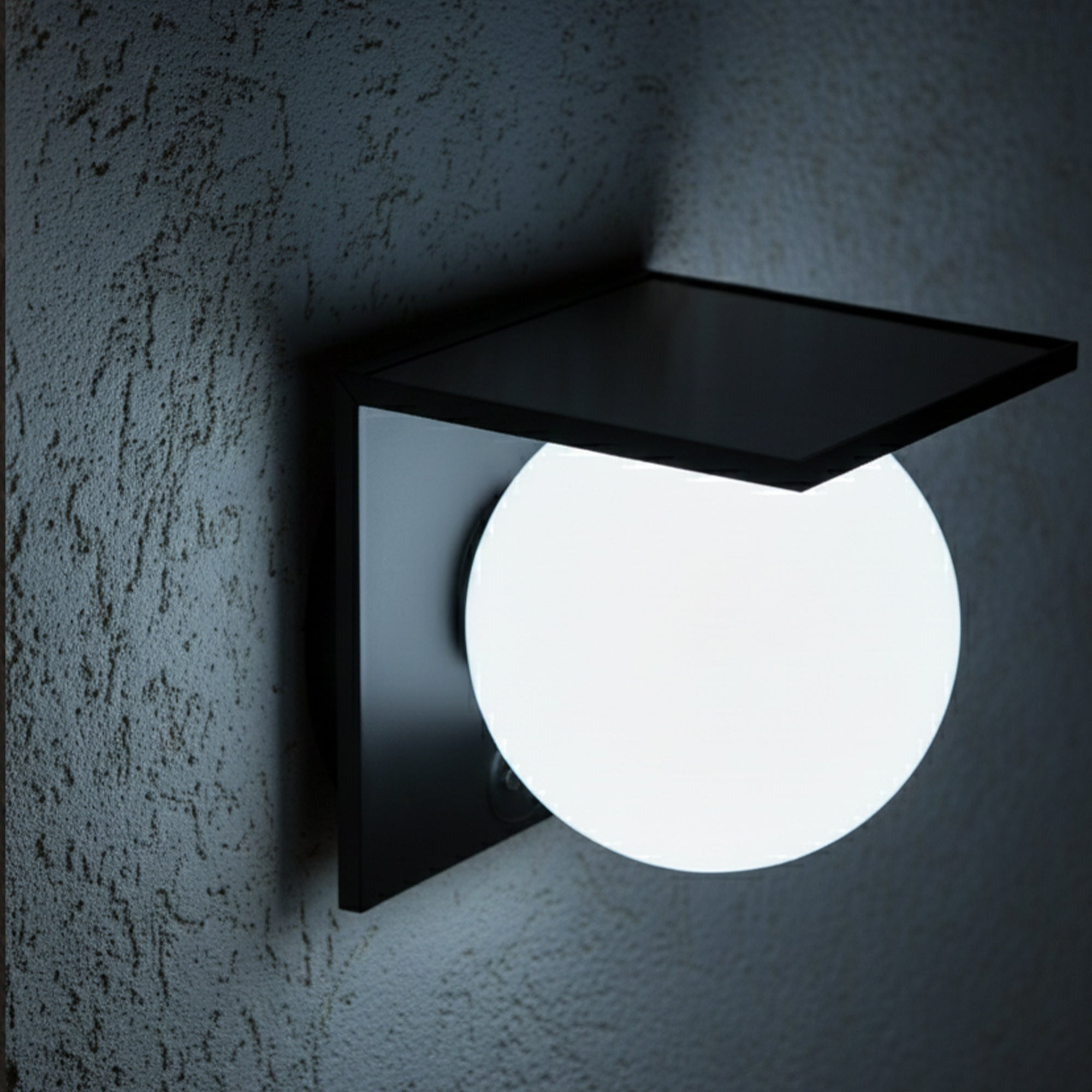 Eine moderne Wandlampe mit einer leuchtenden weißen Kugel und einem schwarzen rechteckigen Schirm an einer strukturierten Wand.