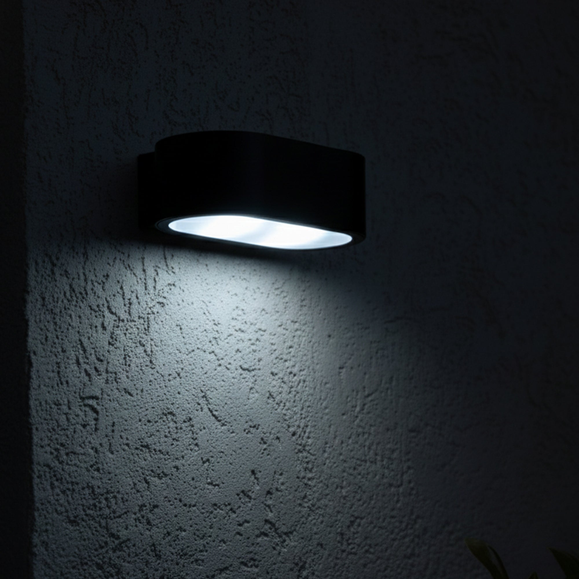 Eine schwarze Wandleuchte ist an einer strukturierten Wand befestigt. Die Lampe strahlt helles Licht nach unten aus.