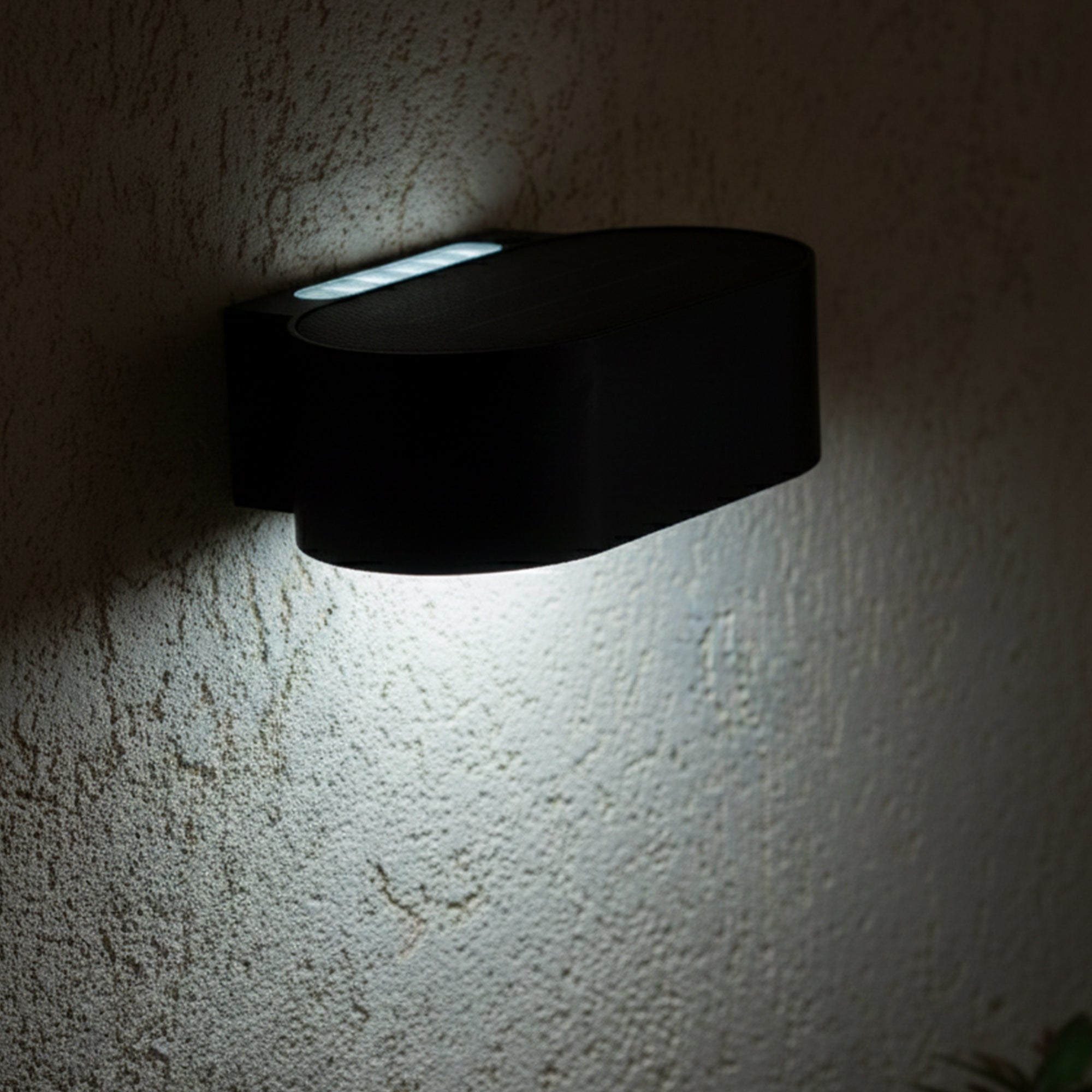 Eine schwarze Wandlampe an einer strukturierten Wand. Die Lampe strahlt helles Licht nach unten aus.