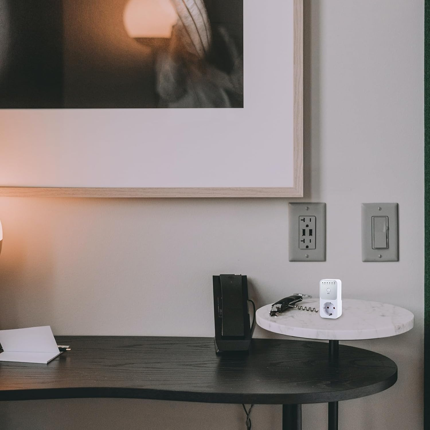 Ein Zimmer mit Schreibtisch, Marmor-Beistelltisch mit Steckdose, gerahmtem Bild und zwei Steckdosen.