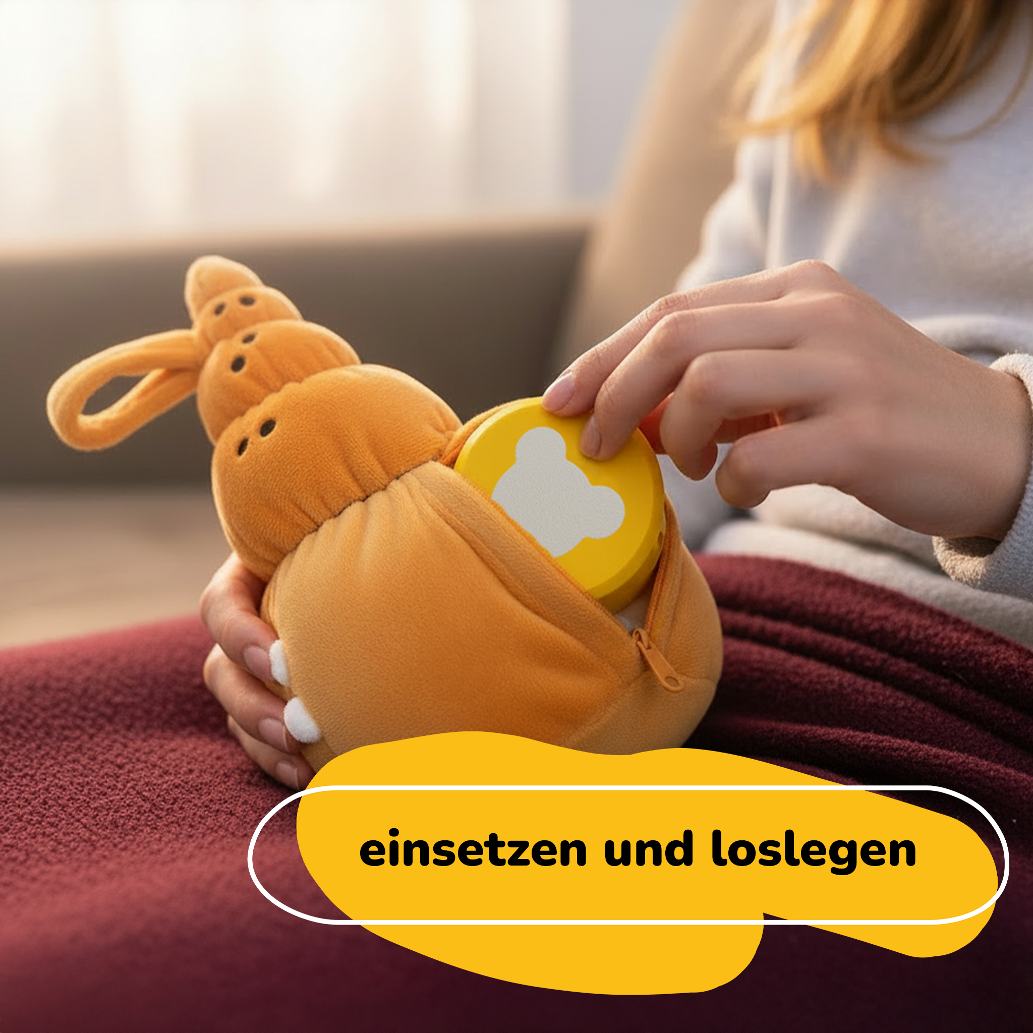 Eine Person hält ein orangefarbenes Plüsch-Schneckenspielzeug. Eine gelbe Scheibe mit Bärenform wird in die Schnecke gesteckt.