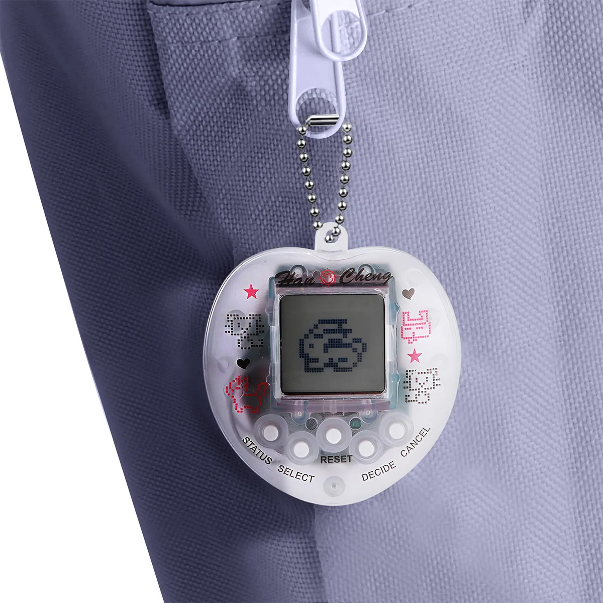 Ein herzförmiges digitales Haustierspielzeug hängt. Es ist mit einem Reißverschluss verbunden. Das Spielzeug hat einen Bildschirm mit einem pixeligen Zeichen.