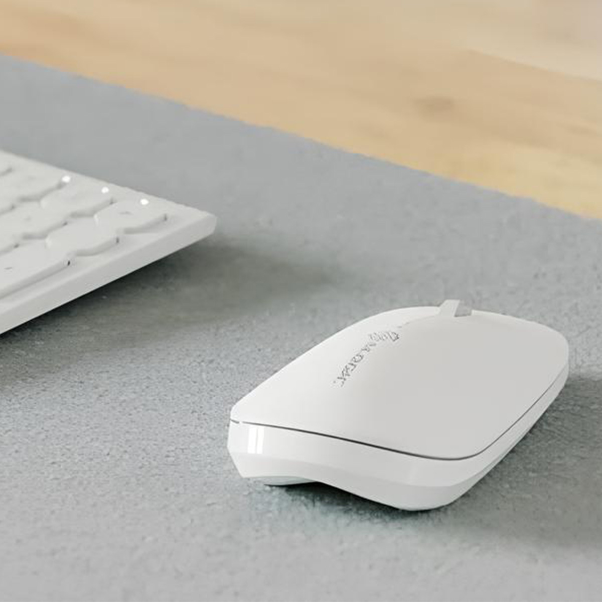Un mouse per computer bianco poggia su una superficie grigia, con una parte di una tastiera bianca visibile sullo sfondo.