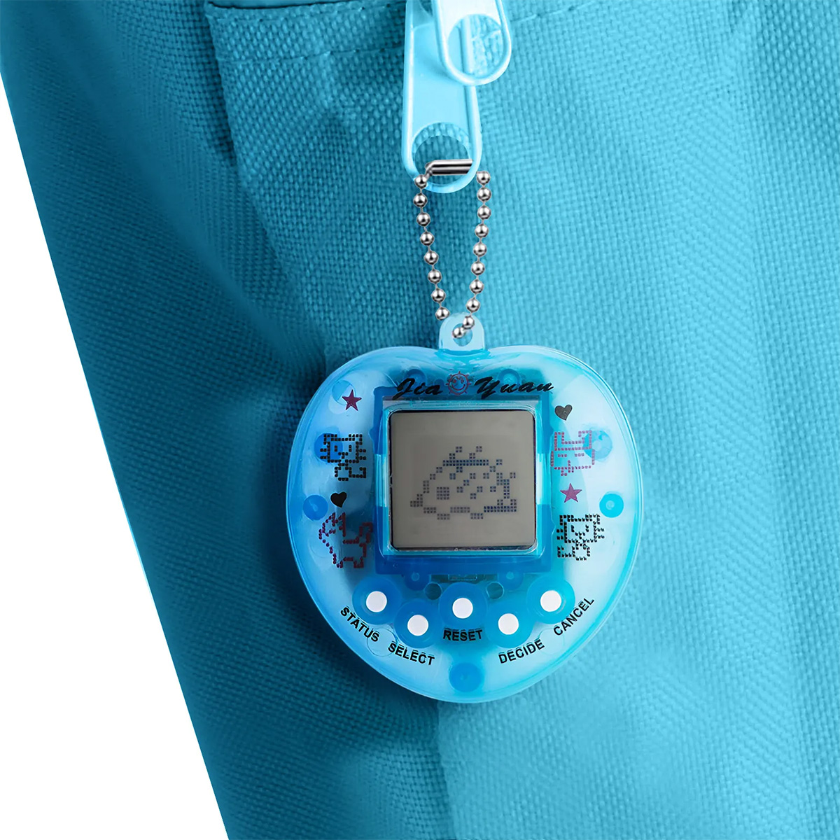 Ein blaues herzförmiges Handheld-Spiel ist an einer blauen Tasche befestigt. Das Spiel zeigt pixelige Charaktere auf dem Bildschirm. Ein blauer Reißverschluss ist sichtbar.