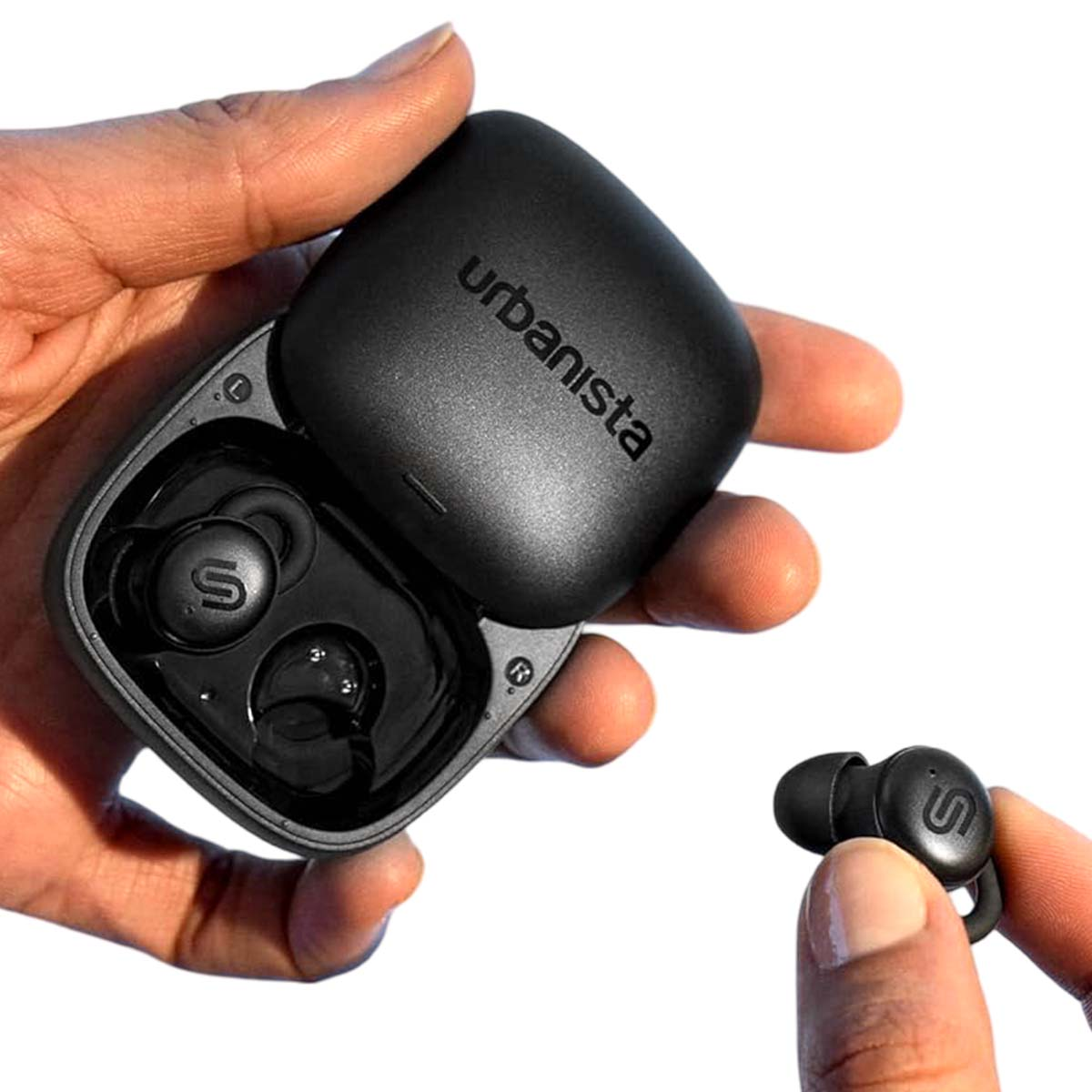 Osoba trzyma czarne etui na słuchawki Urbanista i pojedynczą słuchawkę. Etui jest otwarte, ukazując słuchawki w środku.