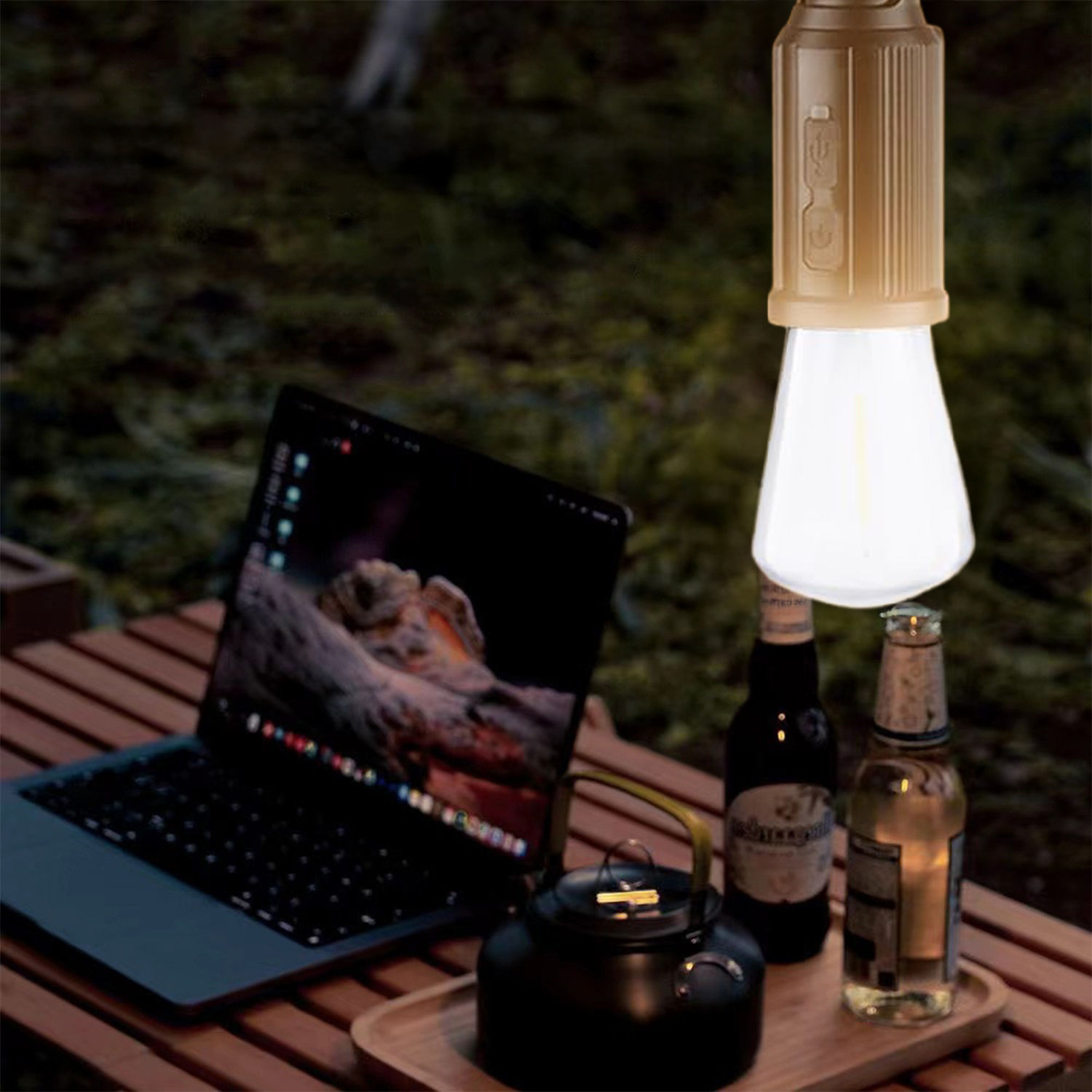 Una lampada accesa è appesa sopra un laptop e bottiglie su un tavolo di legno. Una teiera nera e uno sfondo verde completano la scena.