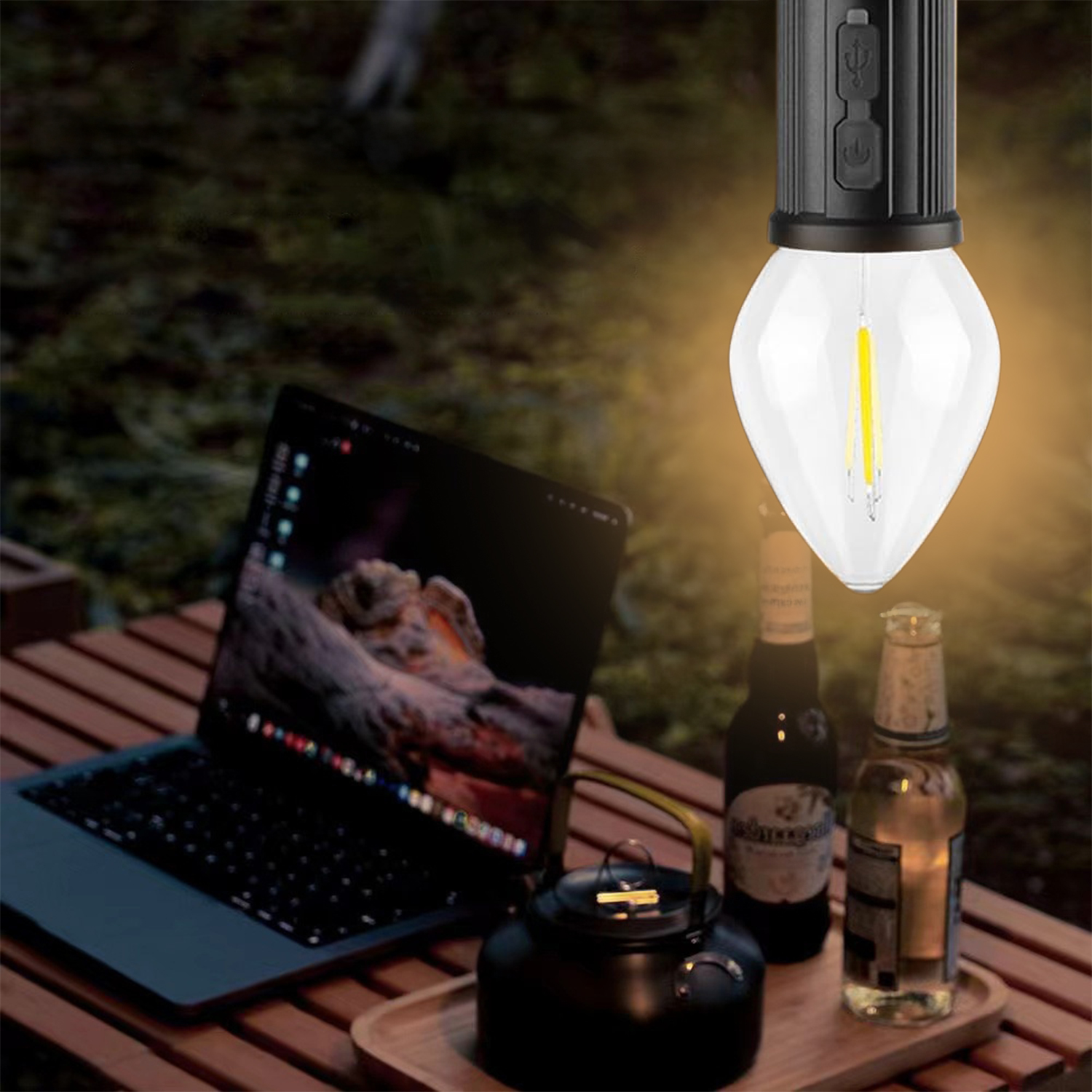 Una lampadina accesa è appesa sopra un laptop, bottiglie e una teiera su un tavolo di legno. Sullo sfondo c'è del verde.