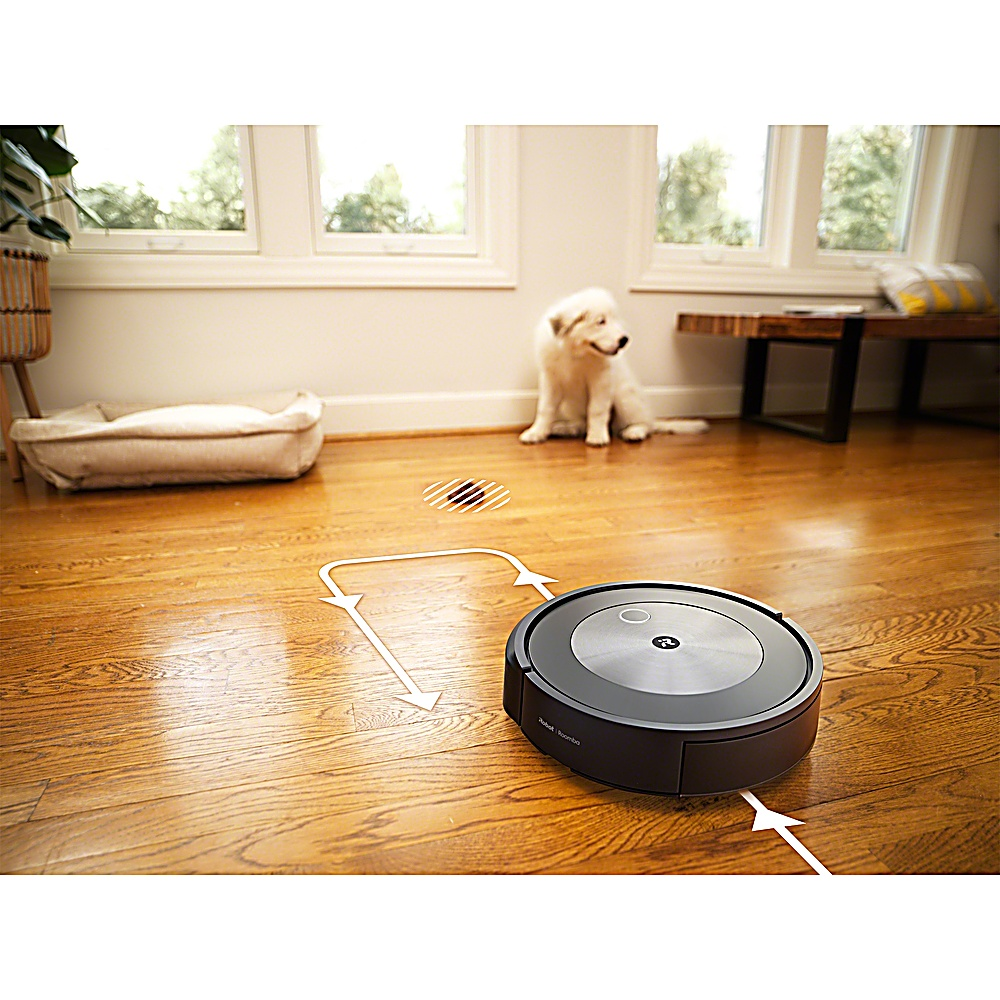 Ein Roboter-Staubsauger reinigt einen Holzboden. Ein weißer Hund sitzt in der Nähe von Fenstern. Ein Hundebett ist links.