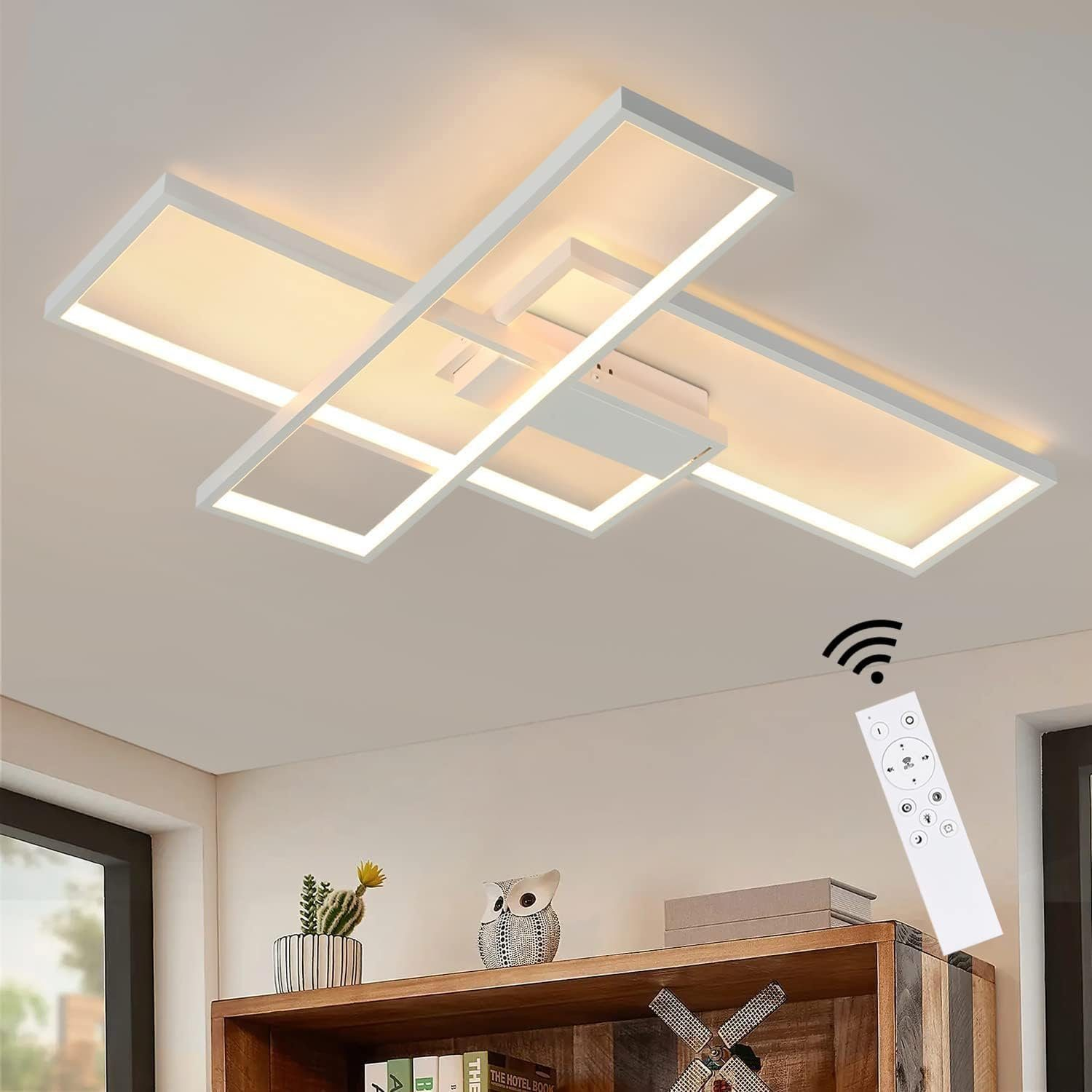 Weiße, geometrische Deckenleuchte mit warmem Schein. Regal unten hat Bücher, Eule und eine Pflanze. Fernbedienung mit WLAN-Signal.